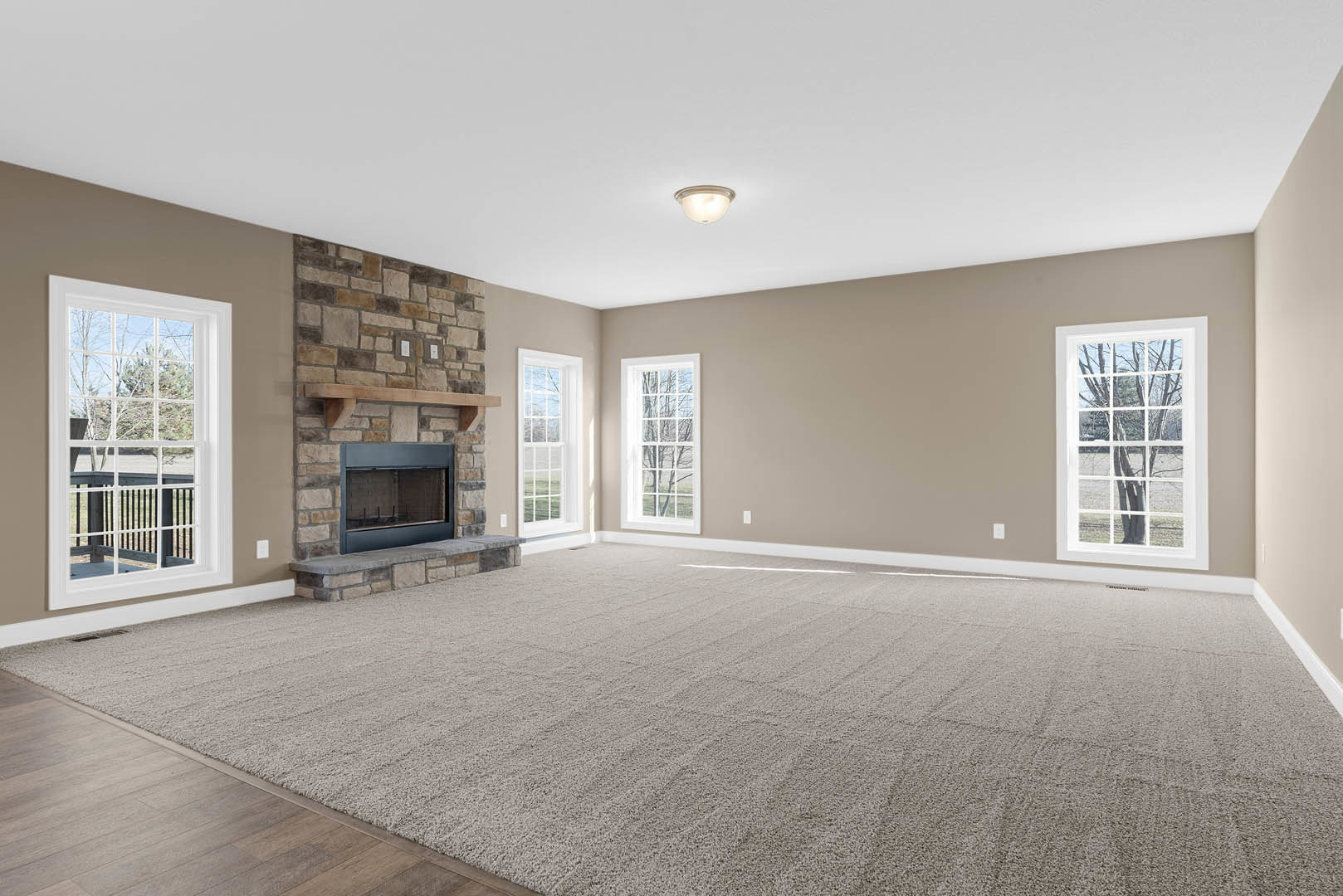 Living room with carpeted floor, glass door fireplace, large window showing trees outside, and staircase leading upstairs