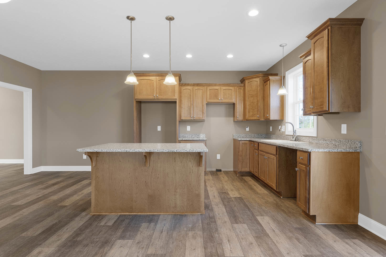Spacious kitchen featuring a large granite island, wood flooring, white cabinetry, tile backsplash, stainless steel sink, and modern fixtures