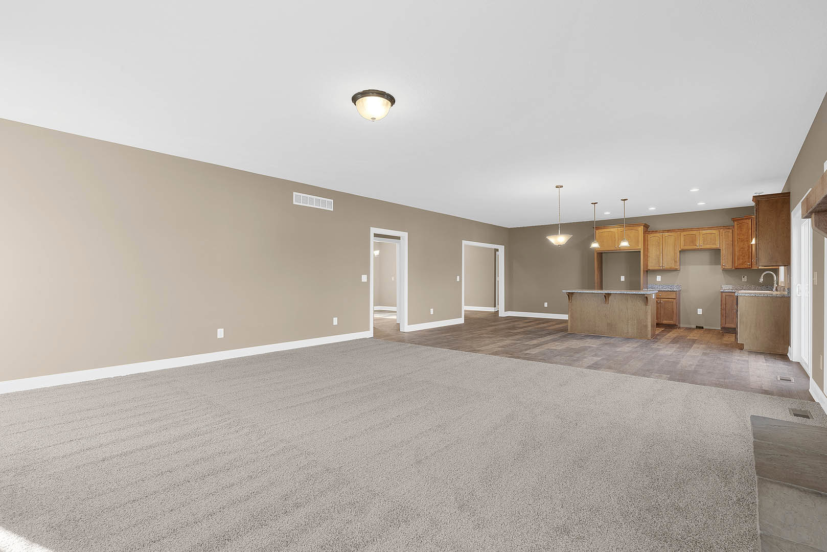 Open concept living room with laminate flooring, white walls, recessed ceiling lights, adjacent kitchen featuring white cabinetry, and dining area with carpeted floor and modern