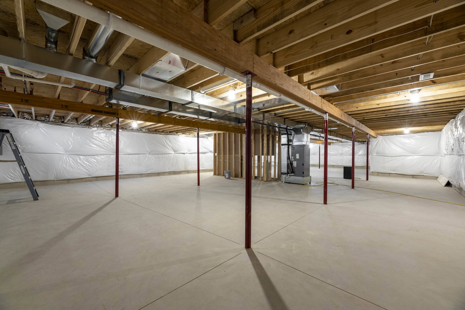 Open room with exposed wood and metal ceiling beams, concrete floor, red support pole, ladder on white surface, and white plastic wall covering
