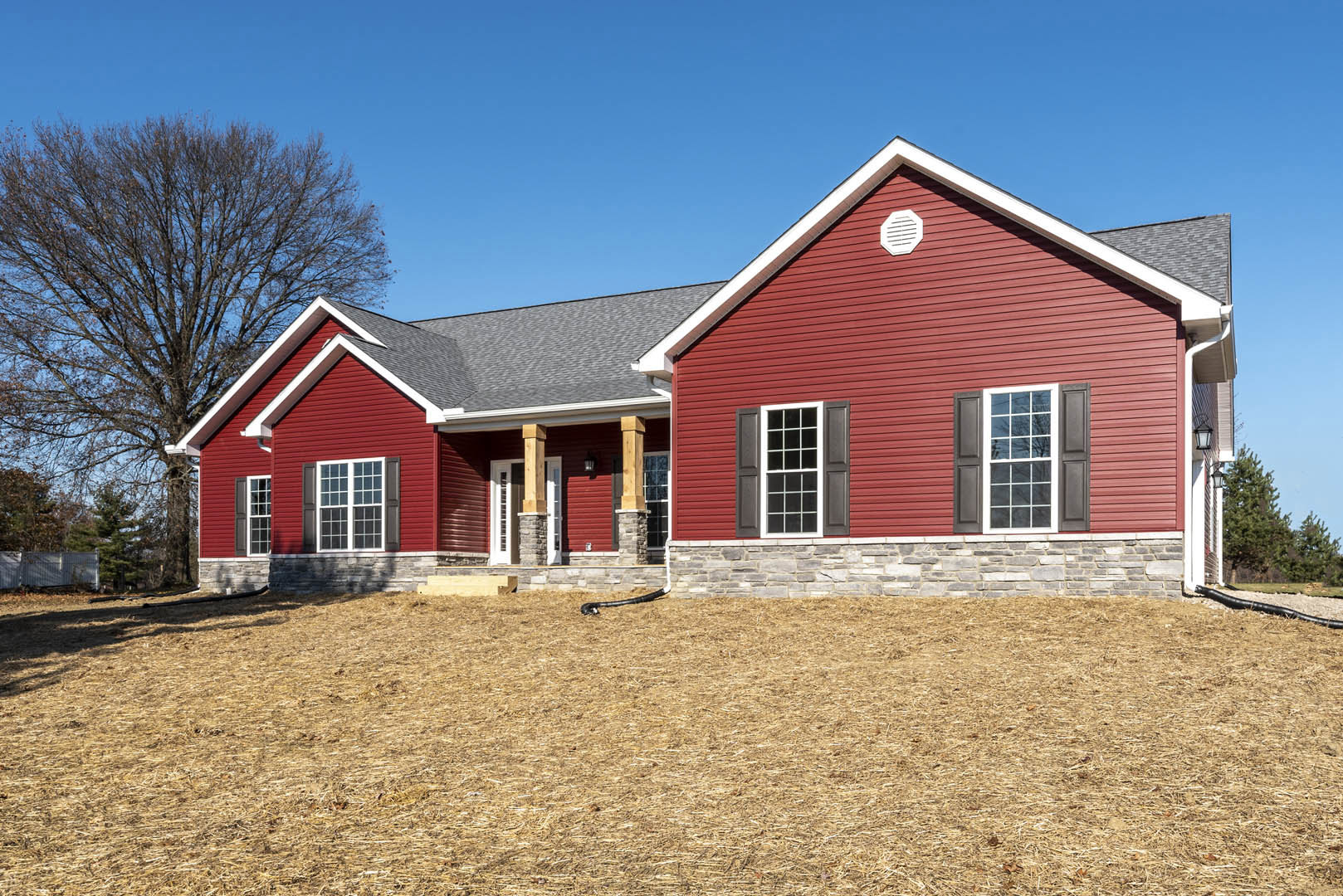 Red house with white trim and stone pillars, grassy hill and tree in background, black snake on lawn, close-up of window and white vent on red siding.
