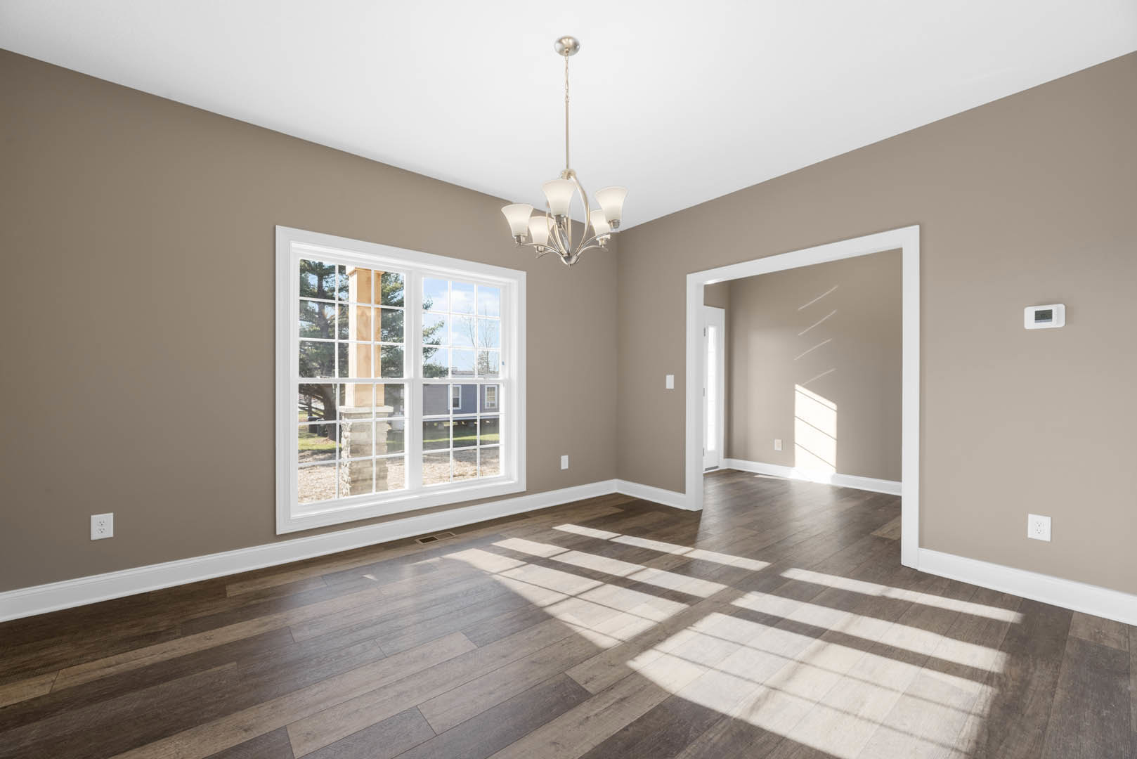 Chandelier hanging from a white ceiling above wood flooring, large windows with white frames, decorative molding, and a ceiling fan with light fixture in a spacious room.