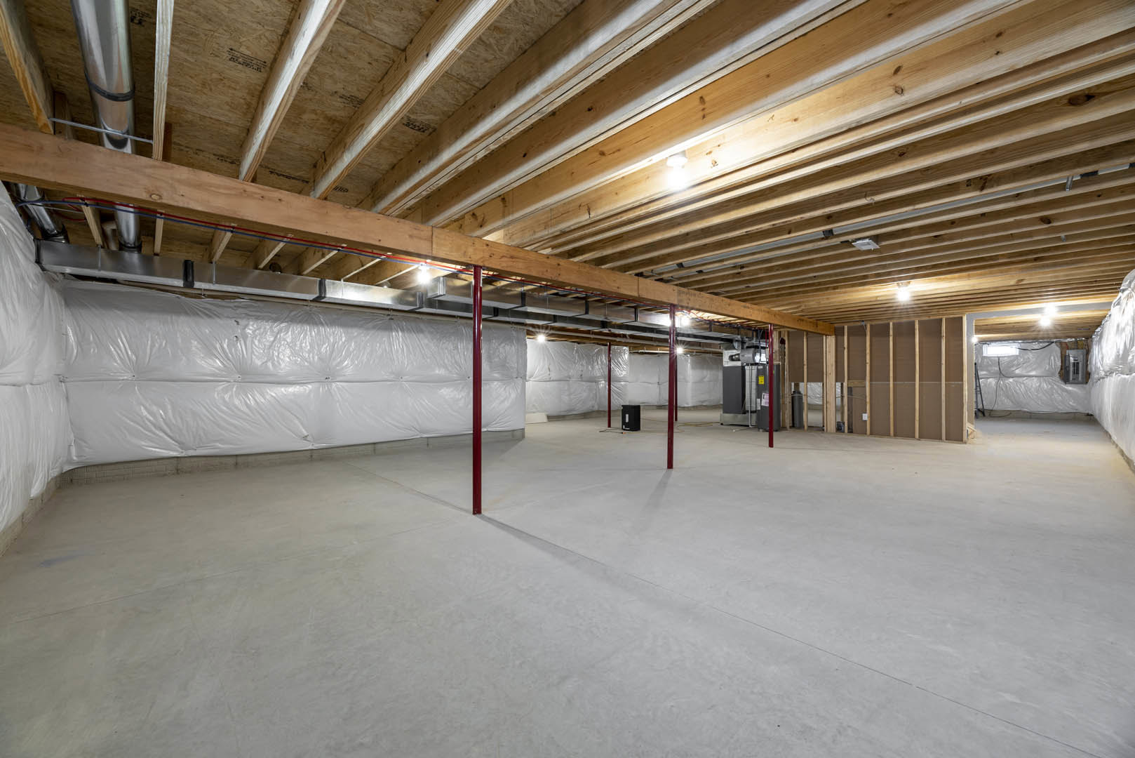 Wooden ceiling with exposed beams, white wall partially covered in plastic, white floor featuring red support poles, close-up of pipe along wall.