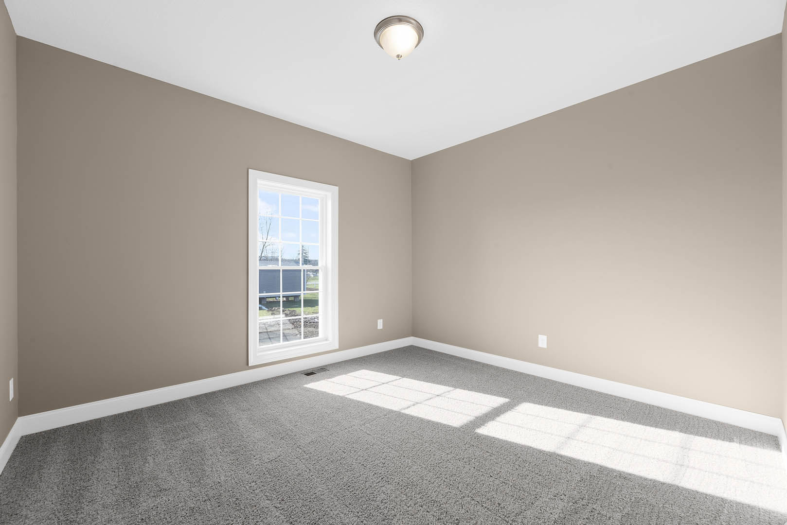 Carpeted room with white walls, large window overlooking neighboring house, ceiling-mounted light fixture, simple molding along ceiling and baseboards