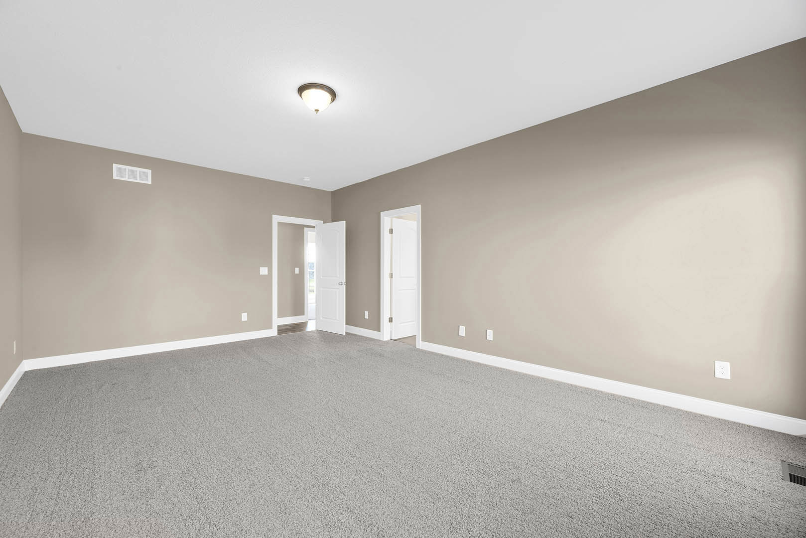 Beige-walled carpeted room with a ceiling light fixture, white door featuring silver handles and a nearby light switch