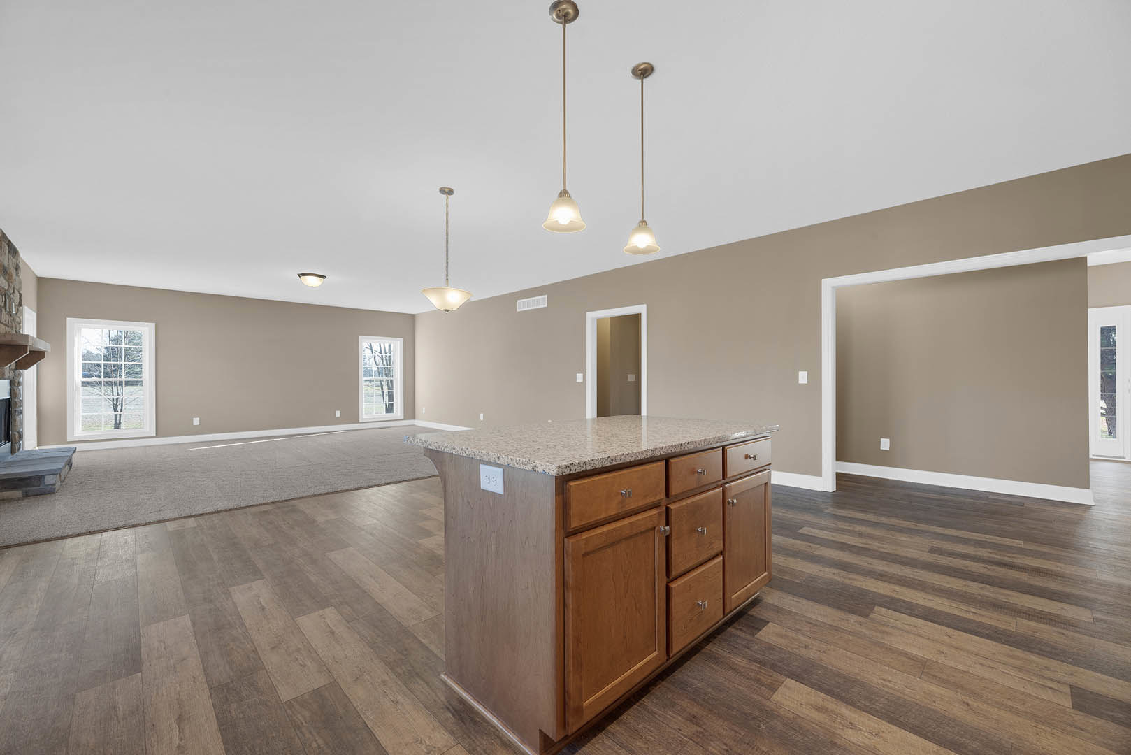 Granite kitchen island with pendant lights in spacious room, white cabinetry, hardwood flooring, large windows overlooking trees
