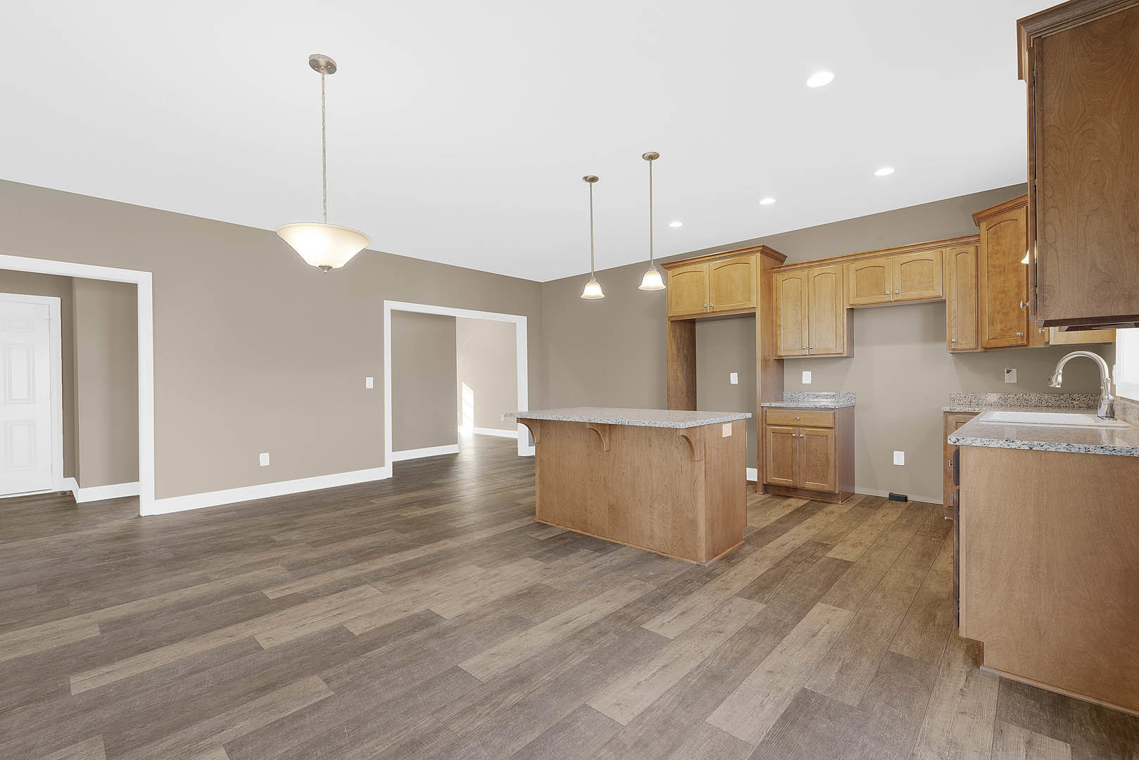 Kitchen with light wood flooring, marble countertop, white cabinetry, and brown-framed door; close-up of wood paneling and countertop visible.