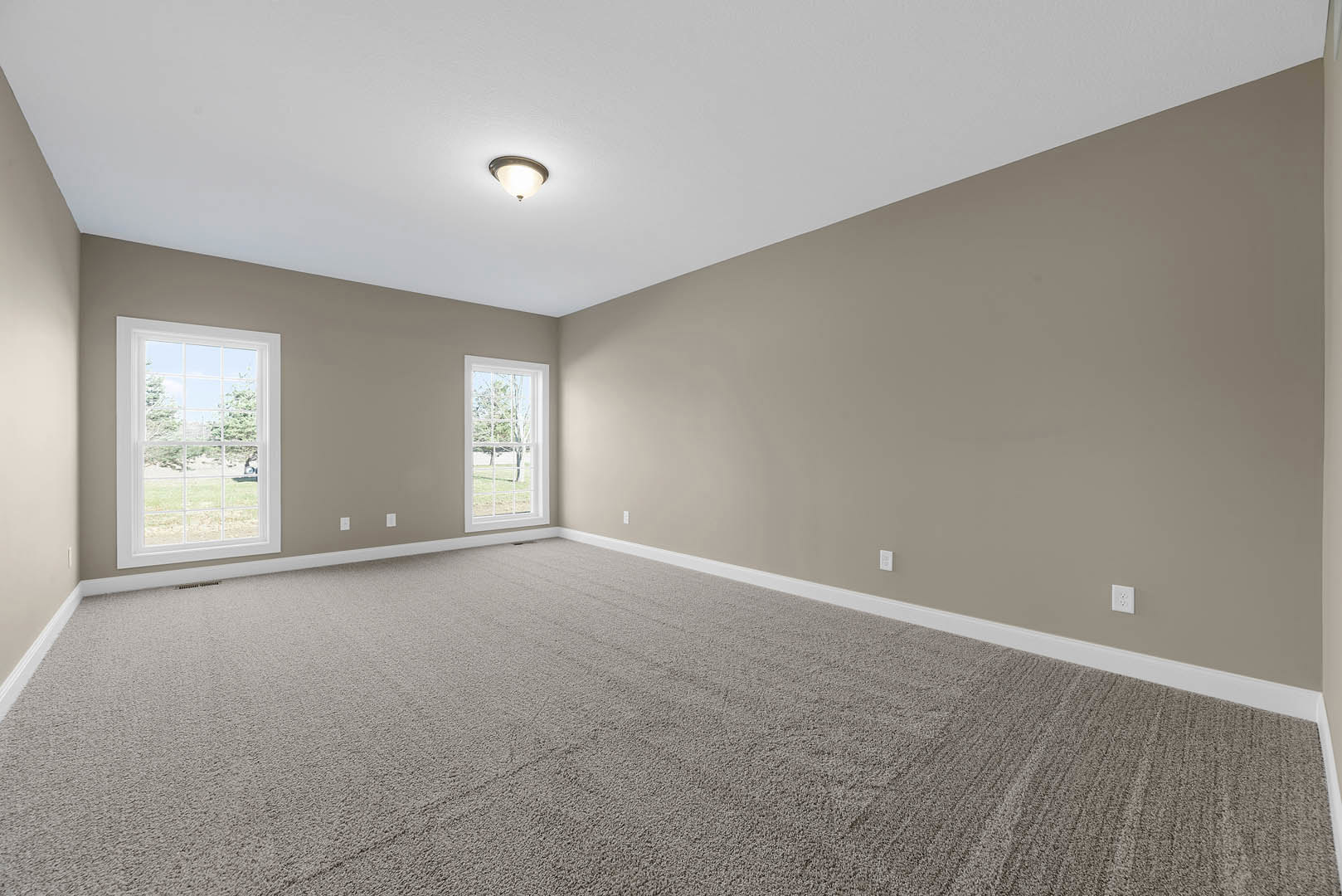 Carpeted room with beige walls, large windows overlooking trees, ceiling light fixture, white molding along baseboards