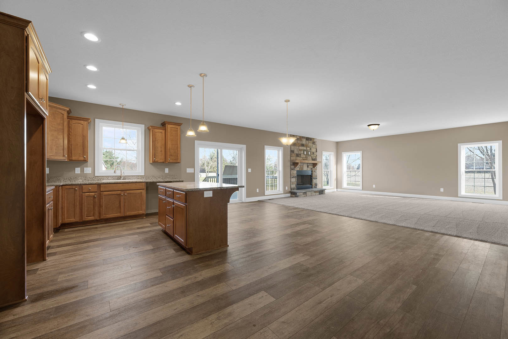 Spacious open floor plan featuring hardwood flooring, central kitchen island with marble countertop, white cabinetry, stainless steel sink, large windows offering views of trees