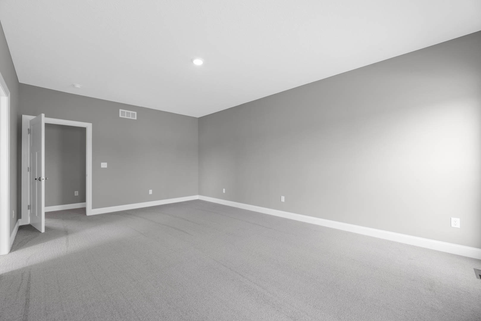 Carpeted room with white ceiling and recessed light, open door featuring silver handle, neutral walls