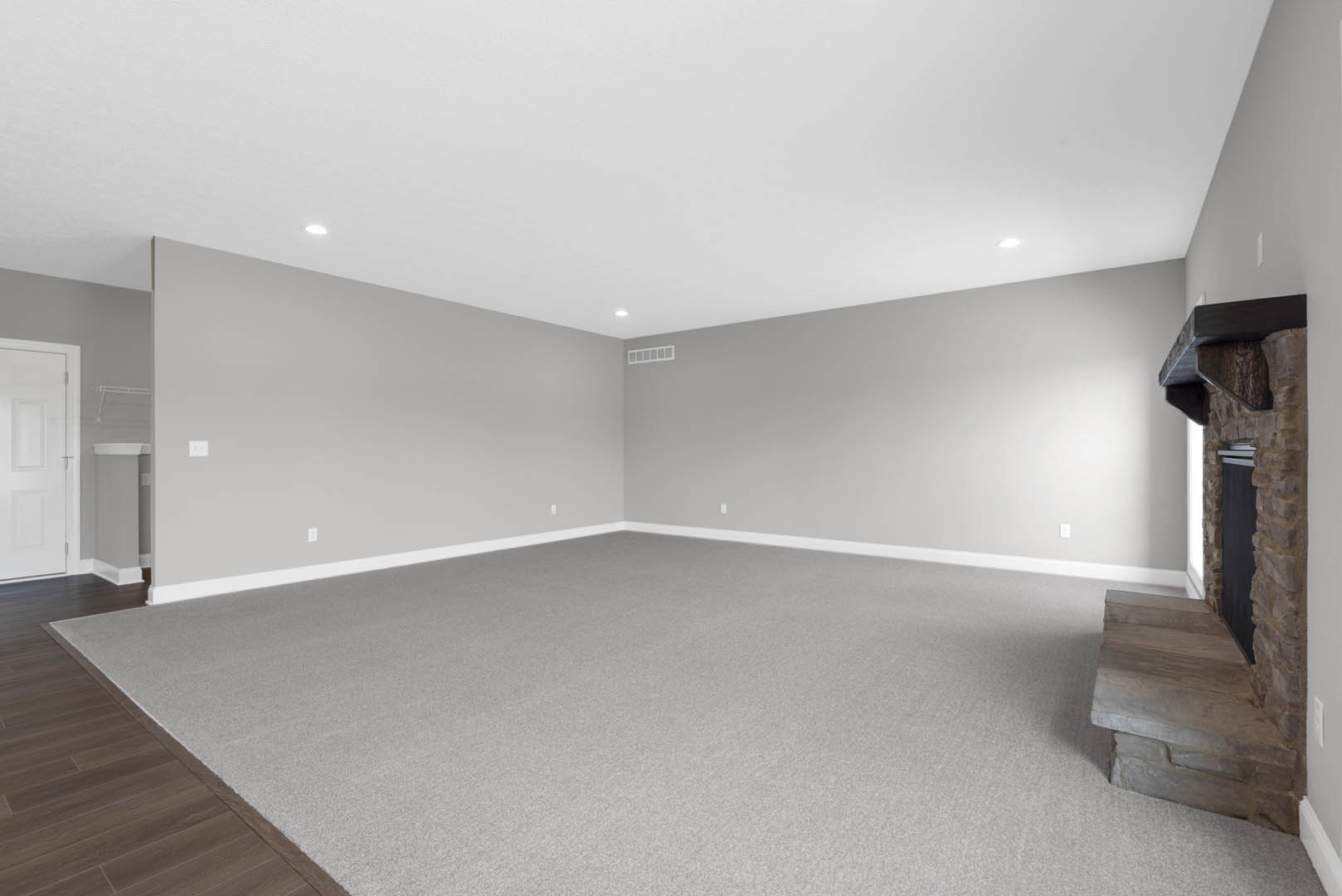 Wooden staircase with natural finish, grey carpeted floor, white door featuring silver handles, stone fireplace with matching stone ledge, bed positioned on carpet, white ceiling