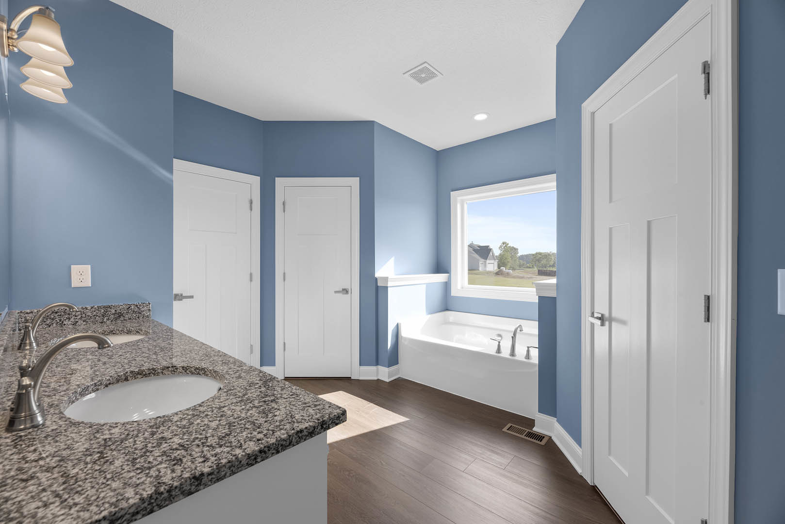 Bathroom featuring a marble countertop with undermount sink, freestanding soaking tub, blue accent wall with white electrical outlet, white door with silver handle, modern lamp