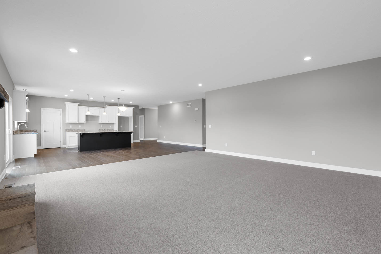 Open kitchen with black and white countertops, wood cabinetry, carpeted floor, white ceiling with recessed lights, and a white door with silver handle