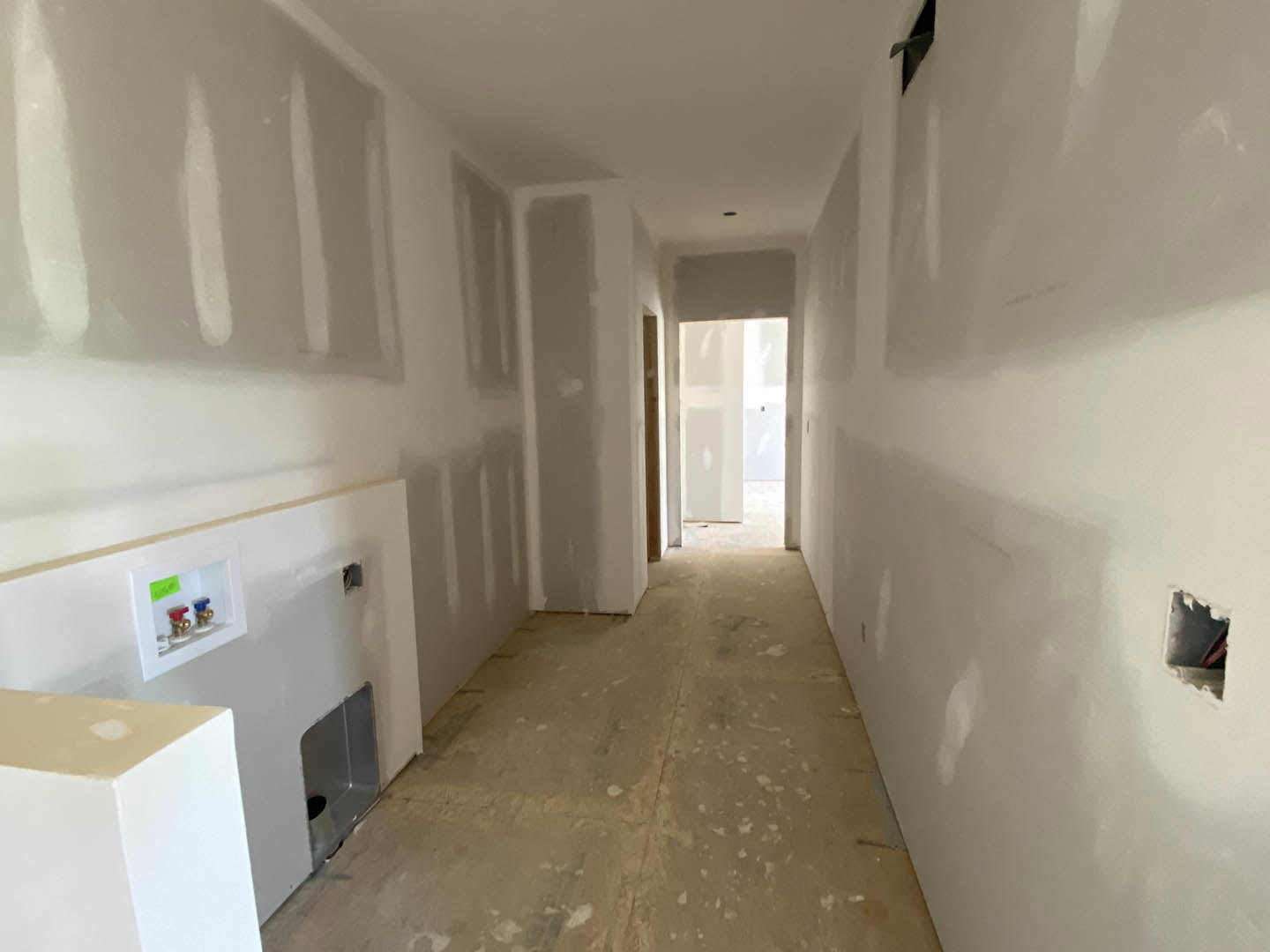 Hallway with smooth white plaster walls, light-colored flooring, and a closed white door at the end