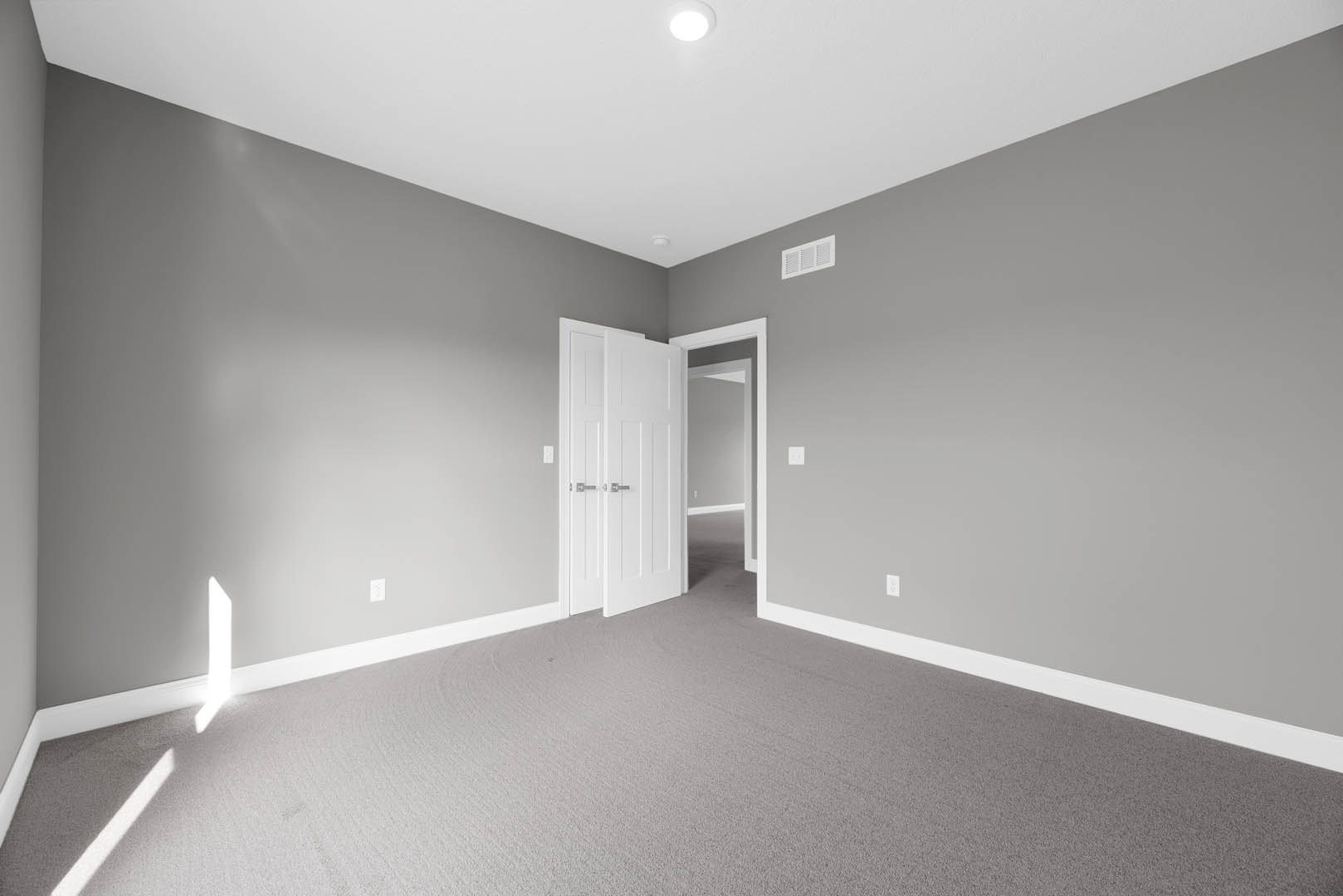 White-walled room with open white door featuring silver handles, ceiling light, white wall vent, and close-up view of light-colored carpet flooring