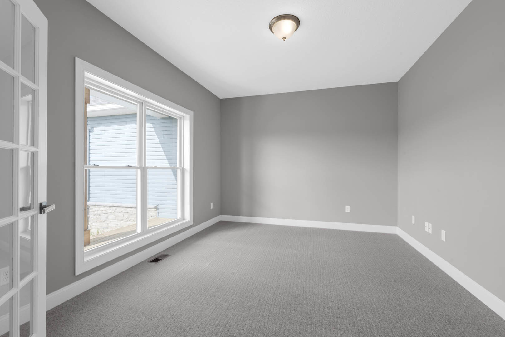 Carpeted room with white walls, white-framed window, ceiling light fixture, and stone accent wall surrounding the window