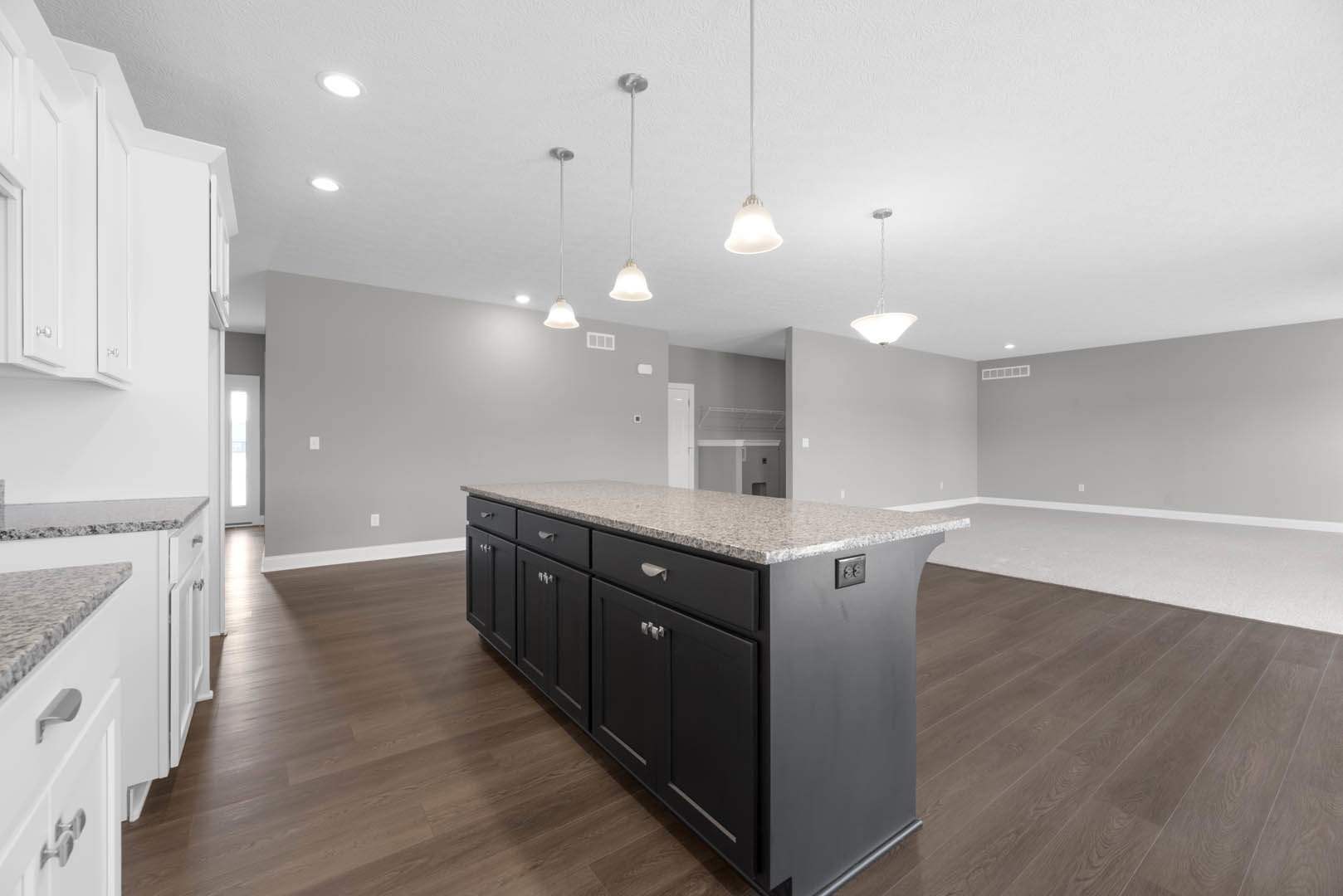 Granite kitchen island with white cabinetry, stainless steel sink, pendant light fixtures, and hardwood flooring
