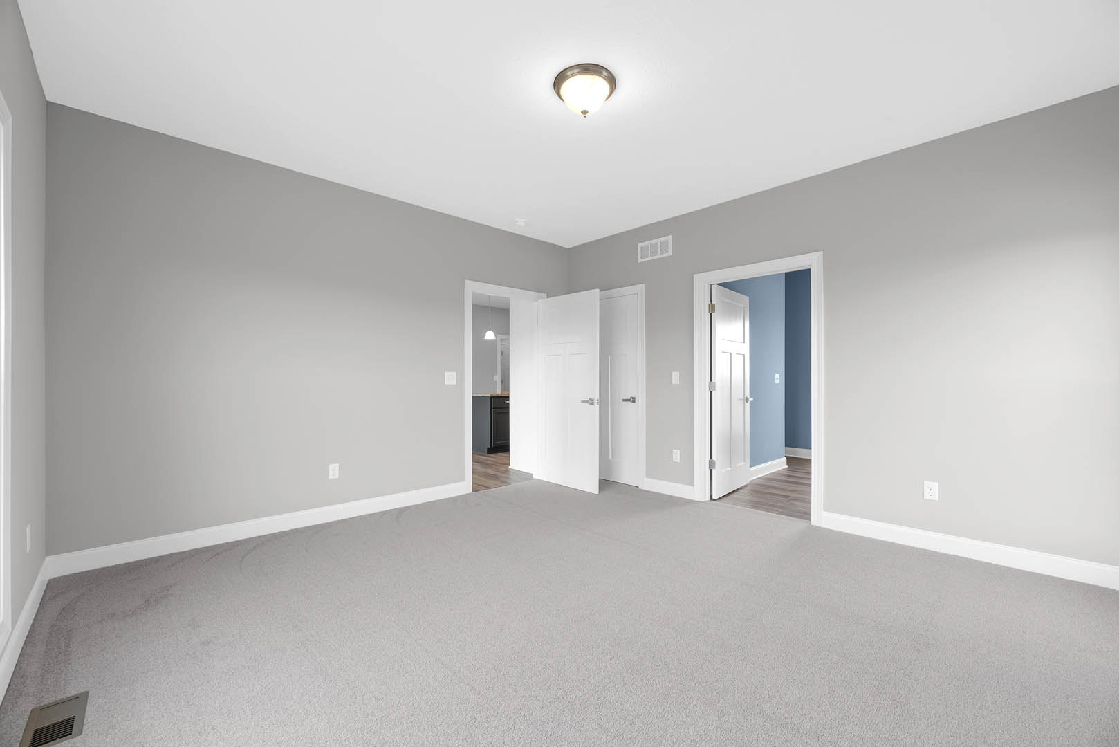 White-walled room with a ceiling light fixture, white carpet flooring, white door featuring a metal handle, blue accent wall, and grey vent on the ceiling