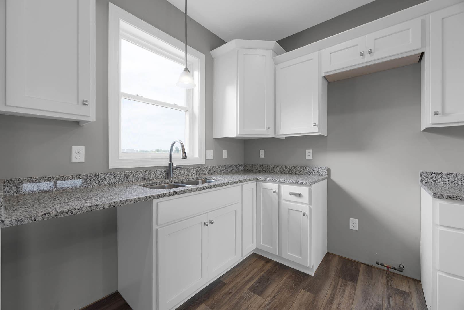 White kitchen cabinets with granite countertops, stainless steel faucet, ceiling light fixture, white electrical outlet on wall, white door with black handle, and modern