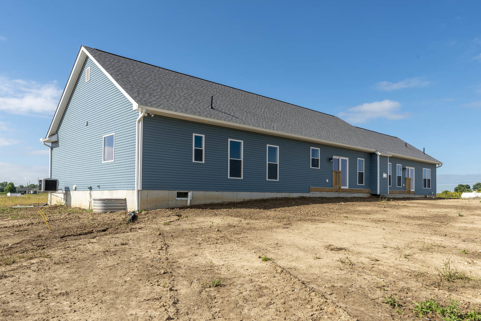 Blue house with white-framed windows set beside a dirt field under a partly cloudy sky