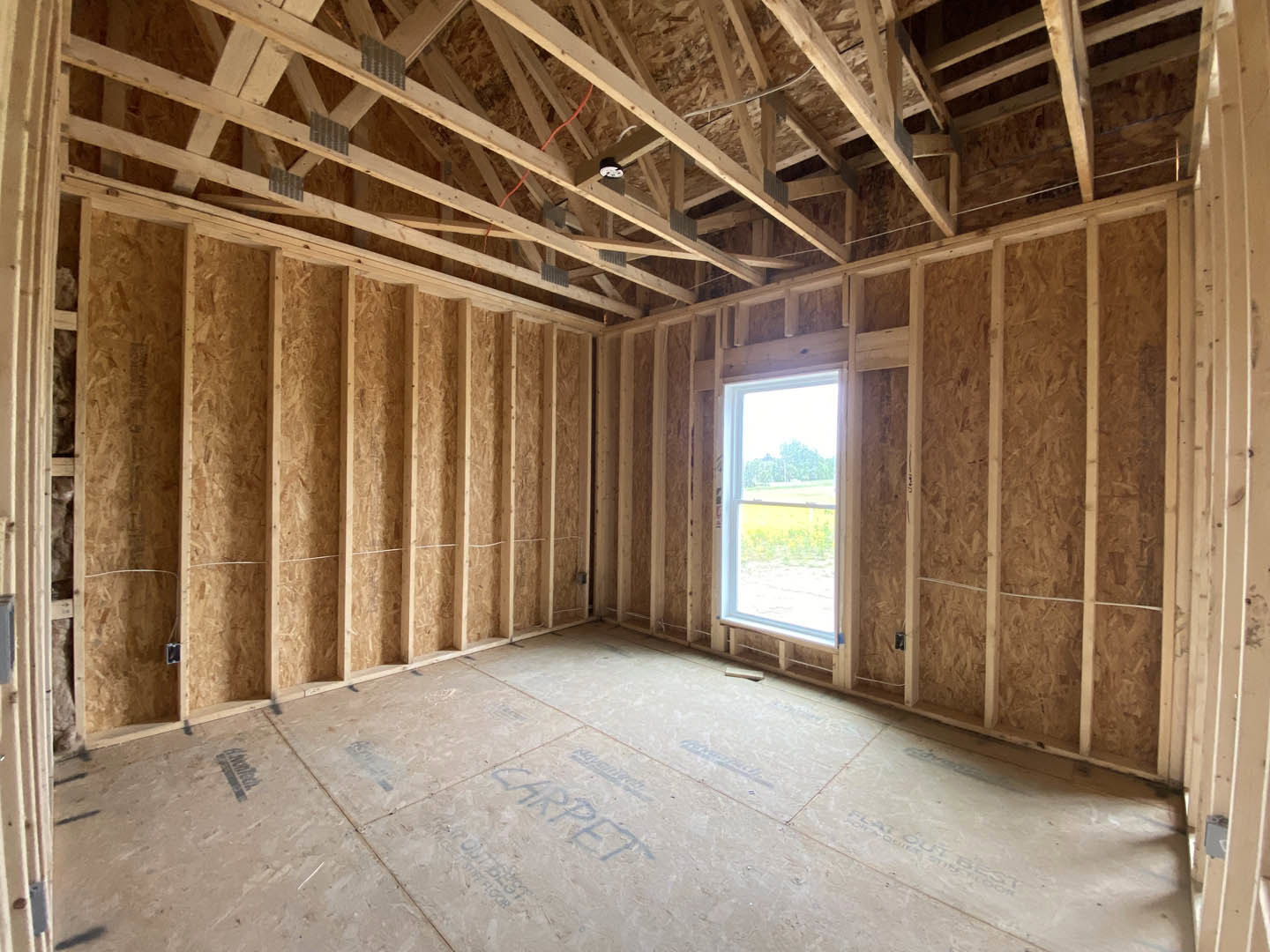 Bright room featuring two large windows centered on a white wall, exposed wood ceiling beams, light plank flooring, and visible building insulation along the upper walls.