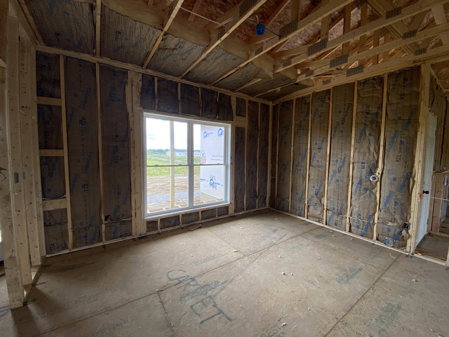 Bright room with two large windows, exposed wood beams, light plank flooring, and visible ceiling insulation