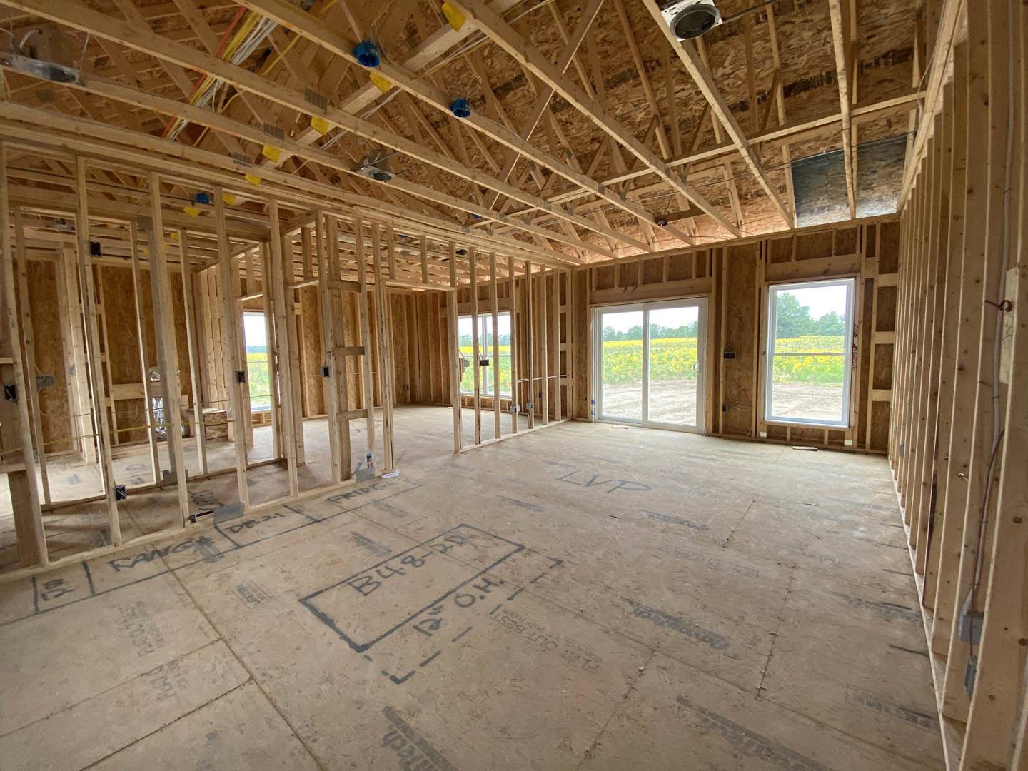 Living room with exposed wood ceiling beams, large windows overlooking a field of flowers, hardwood flooring, and blue decorative objects on the ceiling.