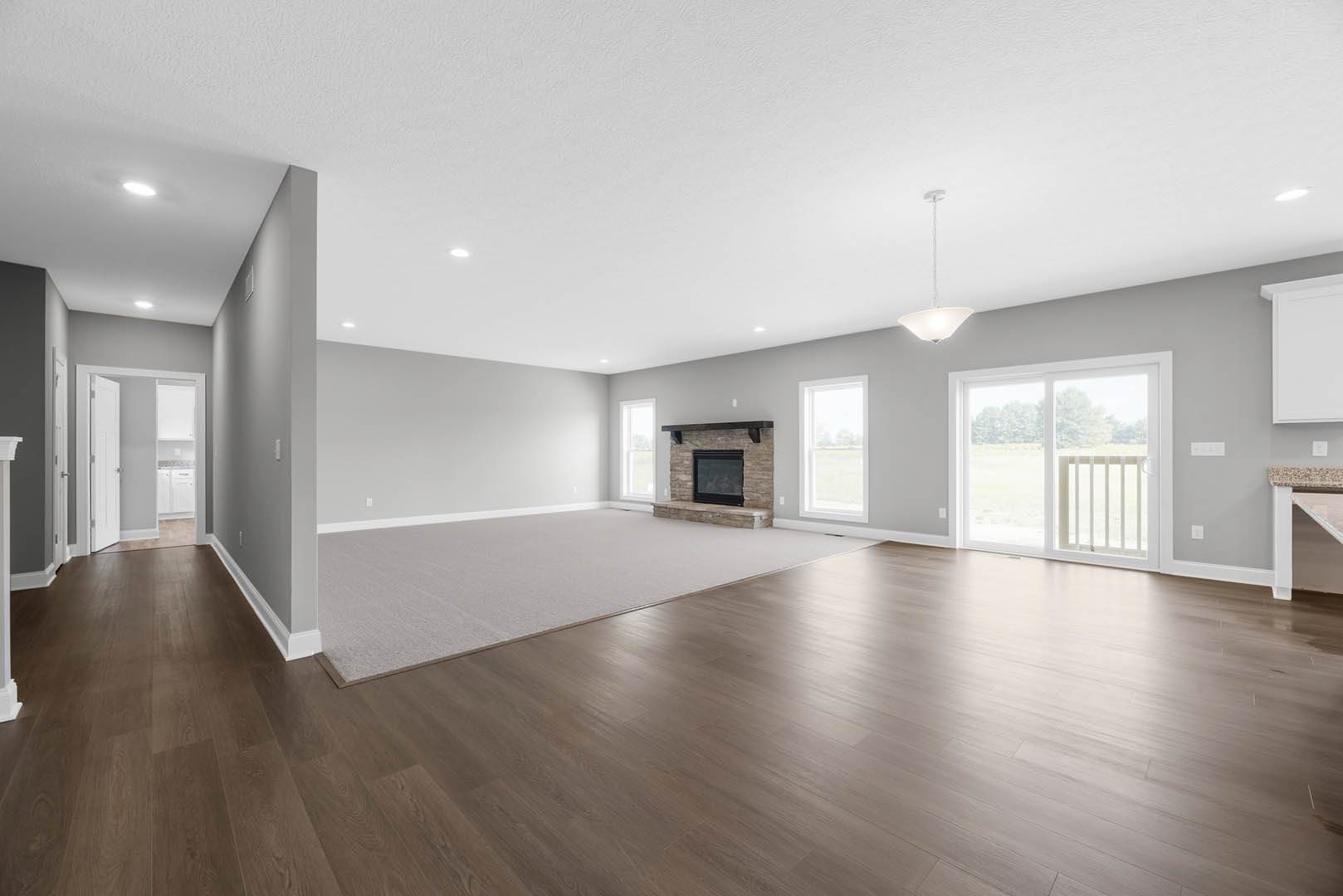 Spacious room with light hardwood flooring, black-framed fireplace, sliding glass door with white railing, and white ceiling pole with light fixture