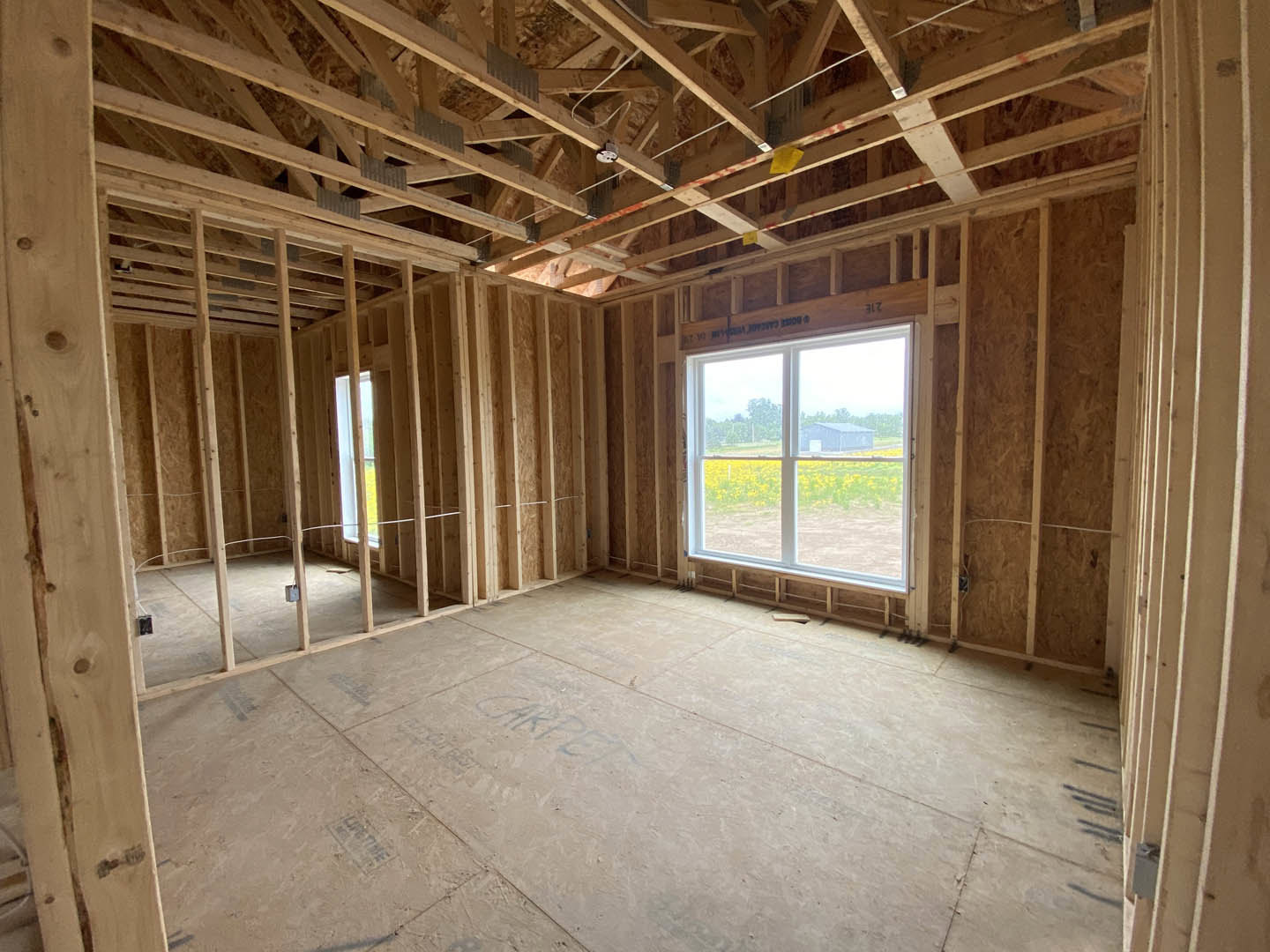 Living room with exposed wood ceiling beams, large windows, and natural light illuminating neutral walls and hardwood flooring