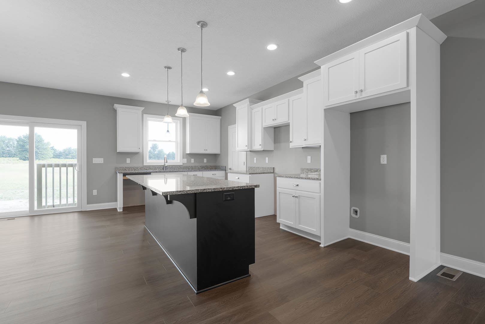 Black kitchen island with waterfall countertop, white shaker cabinets, tile backsplash, stainless steel sink, sliding glass door with white railing, recessed ceiling lights, light
