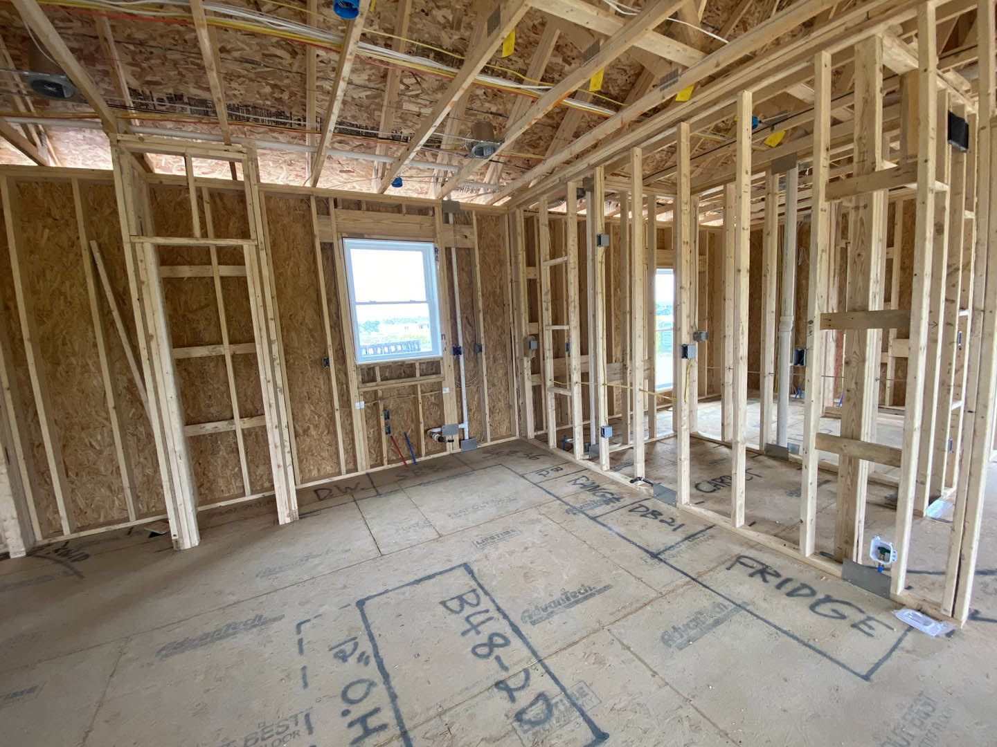 Wood-framed room under construction with exposed beams, white-framed window, concrete floor marked with blue ink and numbers