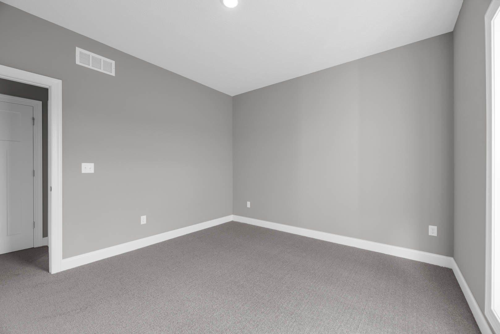 Grey-walled room with light grey carpet, white door featuring metal handle, ceiling vent, and recessed lighting.
