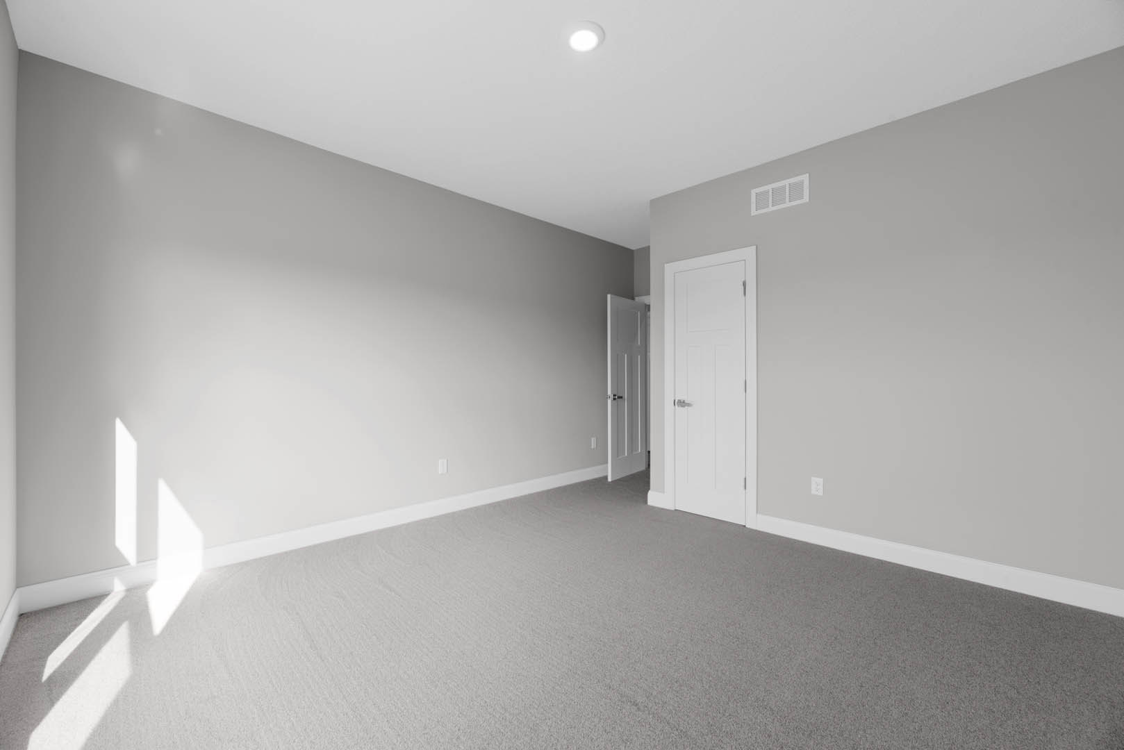 White paneled door with silver handle, beige carpet flooring, white ceiling vent, recessed ceiling light, smooth white walls with simple molding
