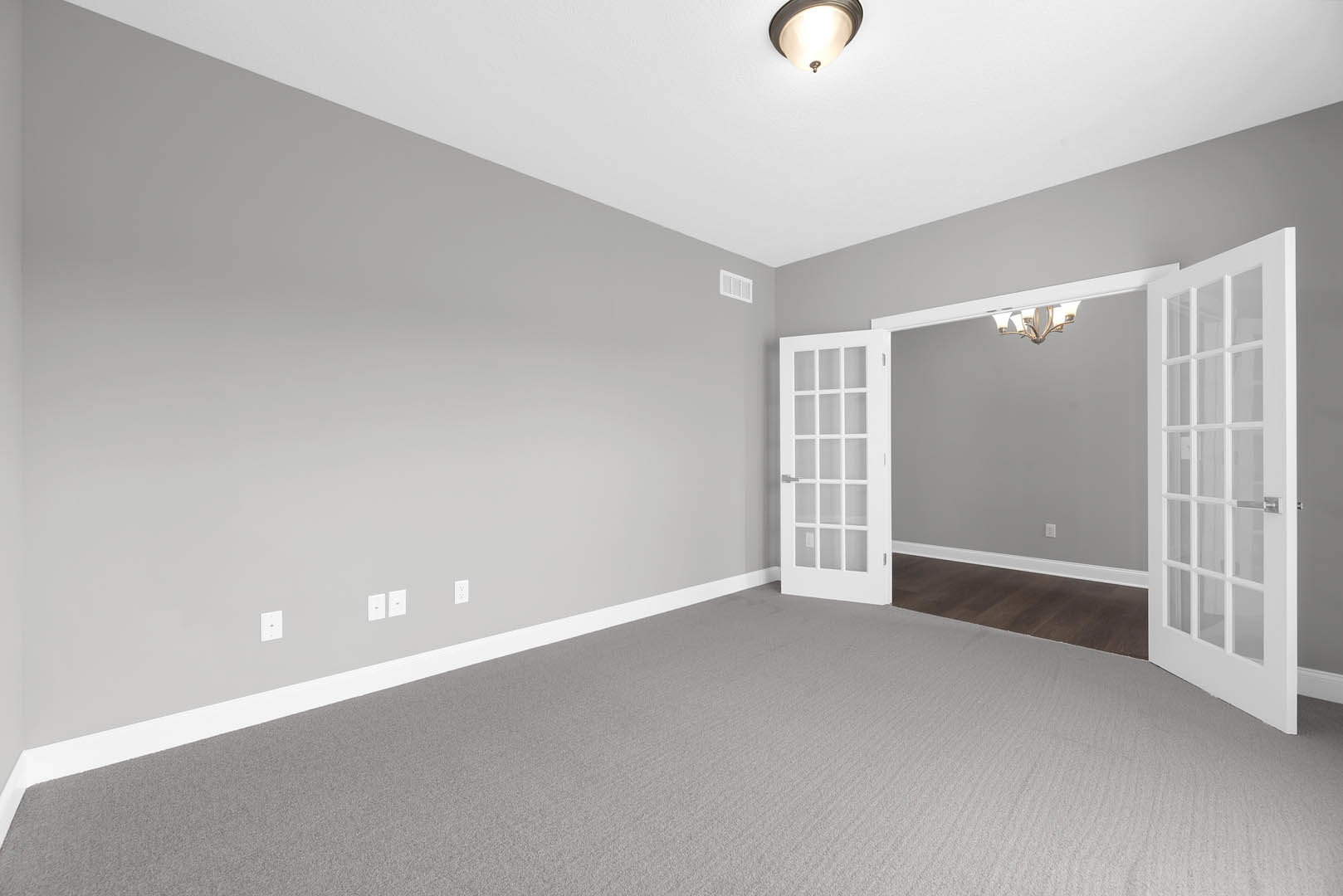 White door with glass panes open to a room featuring grey carpet, wood flooring transition, white plaster walls, ceiling molding, and a modern light fixture.