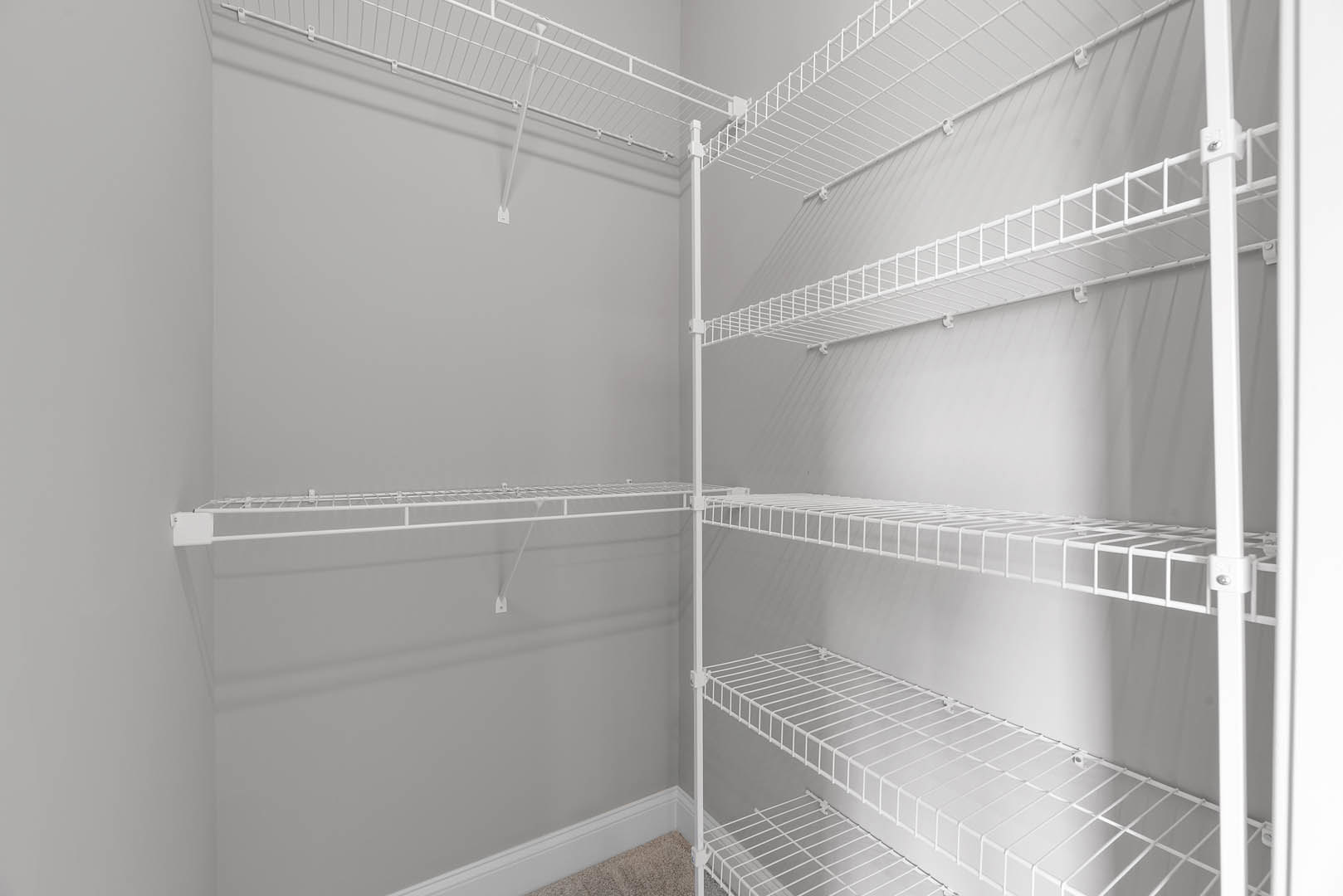 White wire shelving unit mounted on a white wall in a bathroom, with metal racks and ladder-style supports.