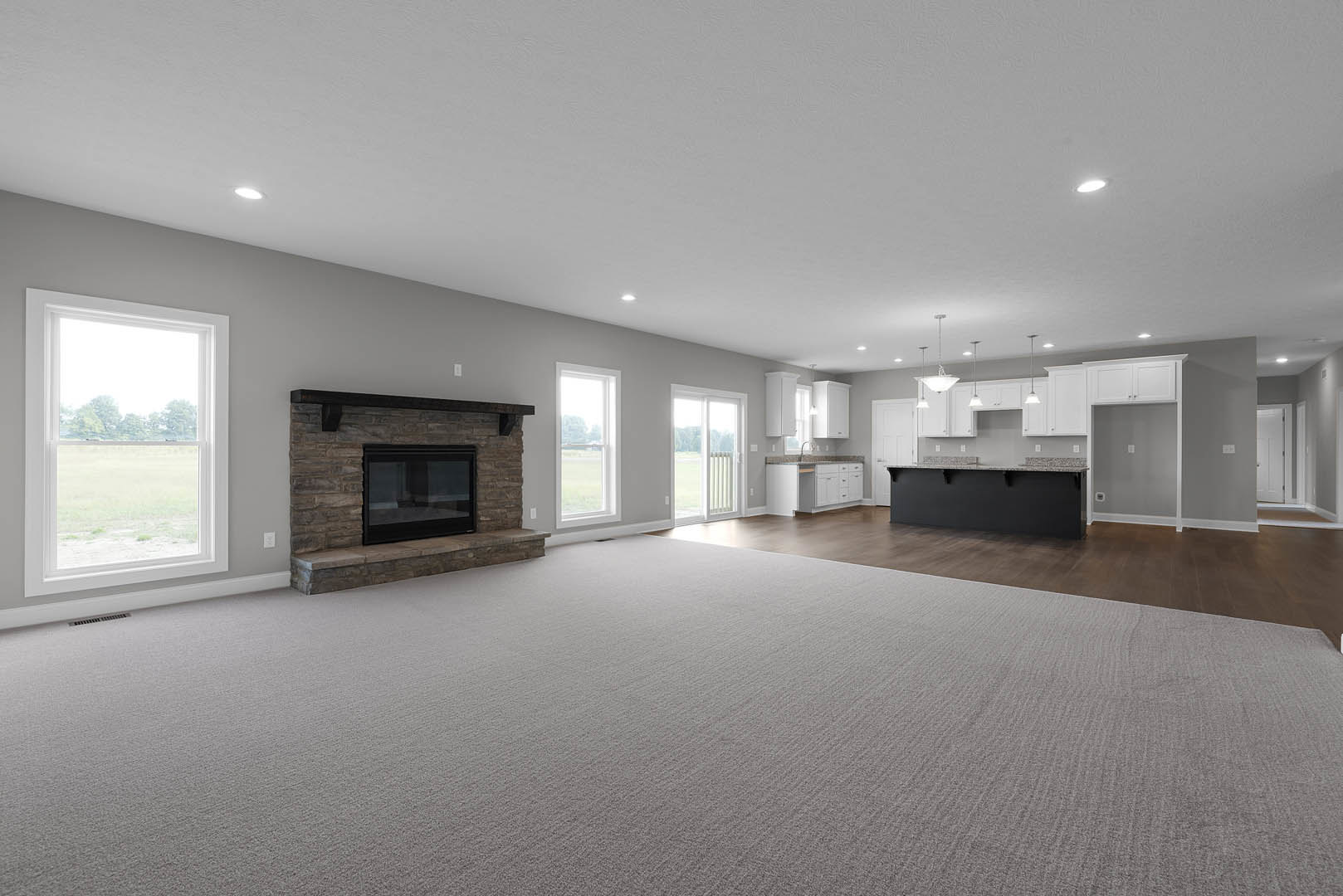 Spacious carpeted living room featuring a black glass-front fireplace, open kitchen area, large window overlooking a field, and white door with window panel.