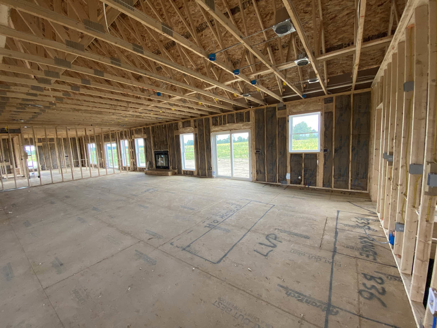 Living room with exposed wooden ceiling beams, concrete floor featuring chalk drawings, modern fireplace, large sliding glass door opening to grassy field, and window framing a