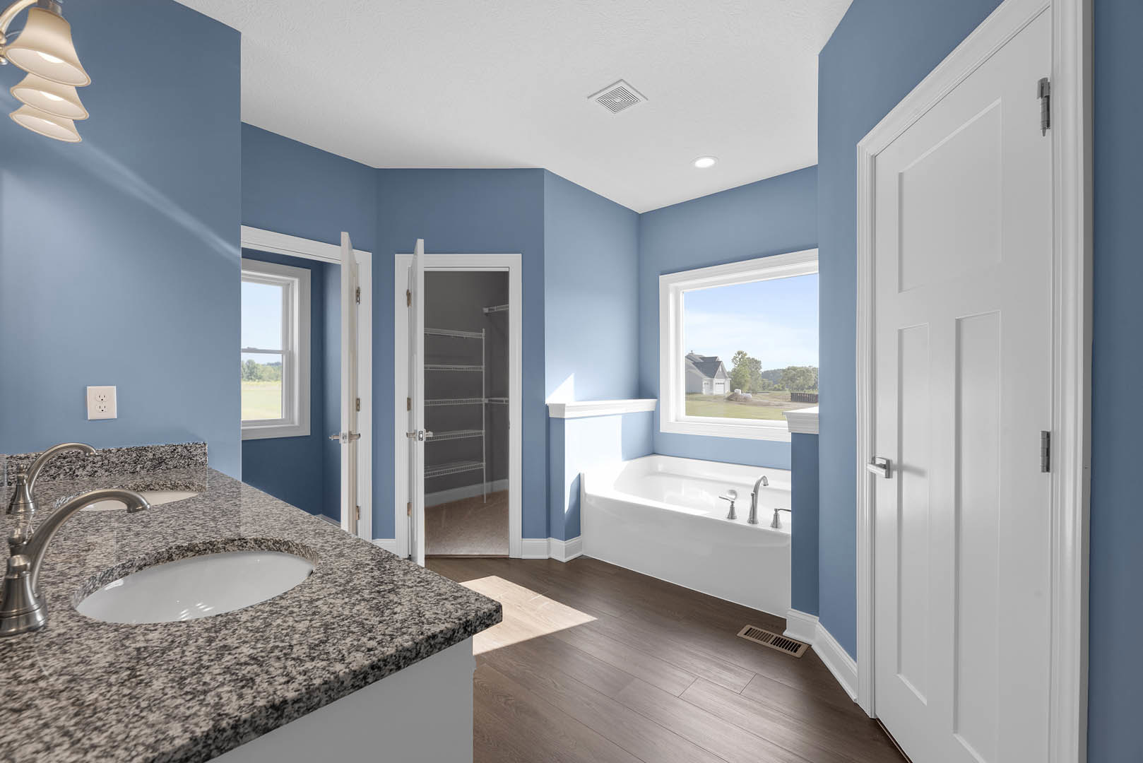 Bathroom featuring a marble countertop with undermount sink, freestanding tub, white door leading to built-in shelving, blue accent wall with white electrical outlet, granite