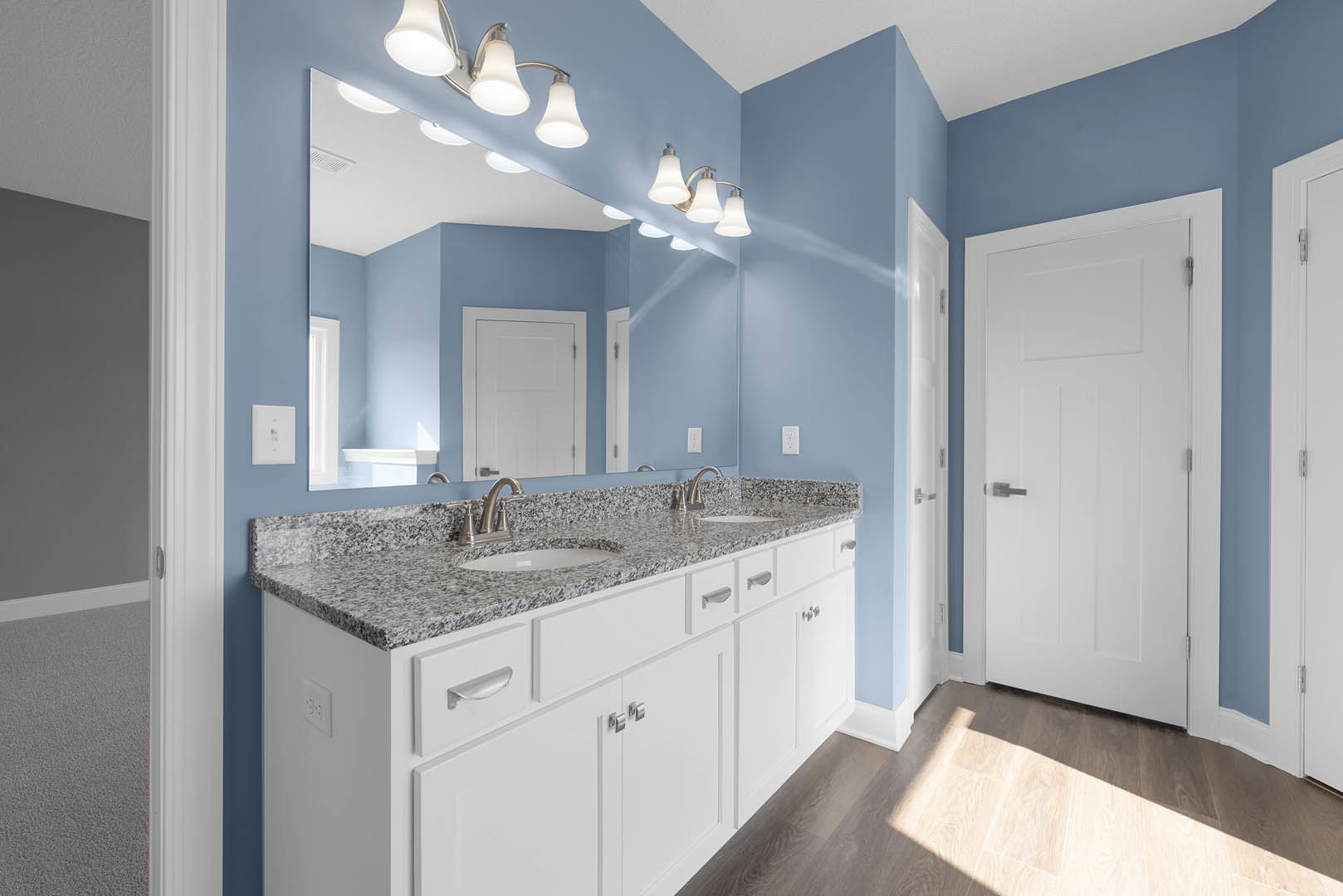 Bathroom with marble countertop, rectangular mirror above sink, white door with silver handle, white walls, ceiling light fixture, and granite sink area.