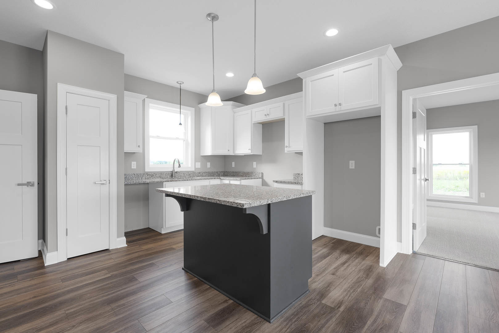 Kitchen with wood flooring, central island featuring marble countertop, white cabinetry, stainless steel sink, window with white frame, white door with silver handle, bell-shaped