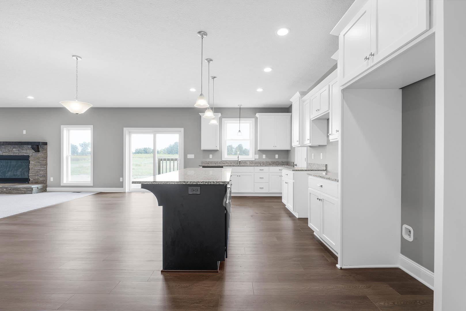 Kitchen featuring white cabinetry, large central island with black countertop, wood laminate flooring, windows overlooking grassy field, and fireplace with black screen