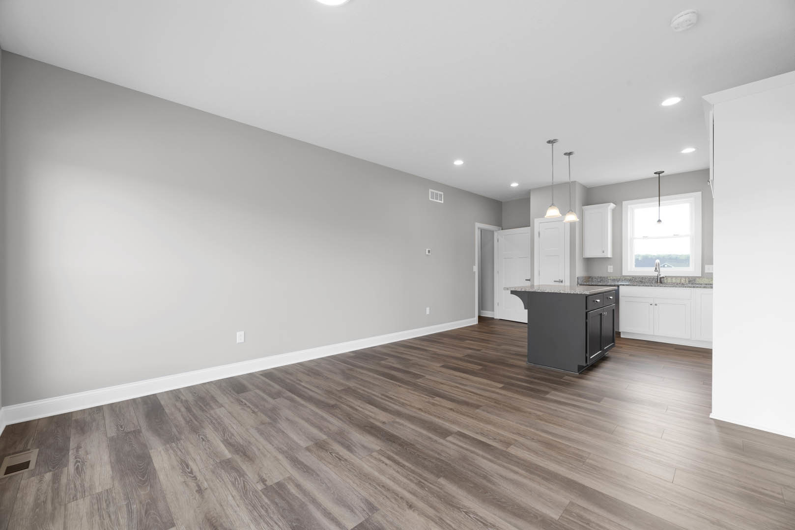 Open kitchen and dining area featuring hardwood floors, white trim, marble-topped kitchen island with built-in sink, vent on wall, and white decorative object on countertop.