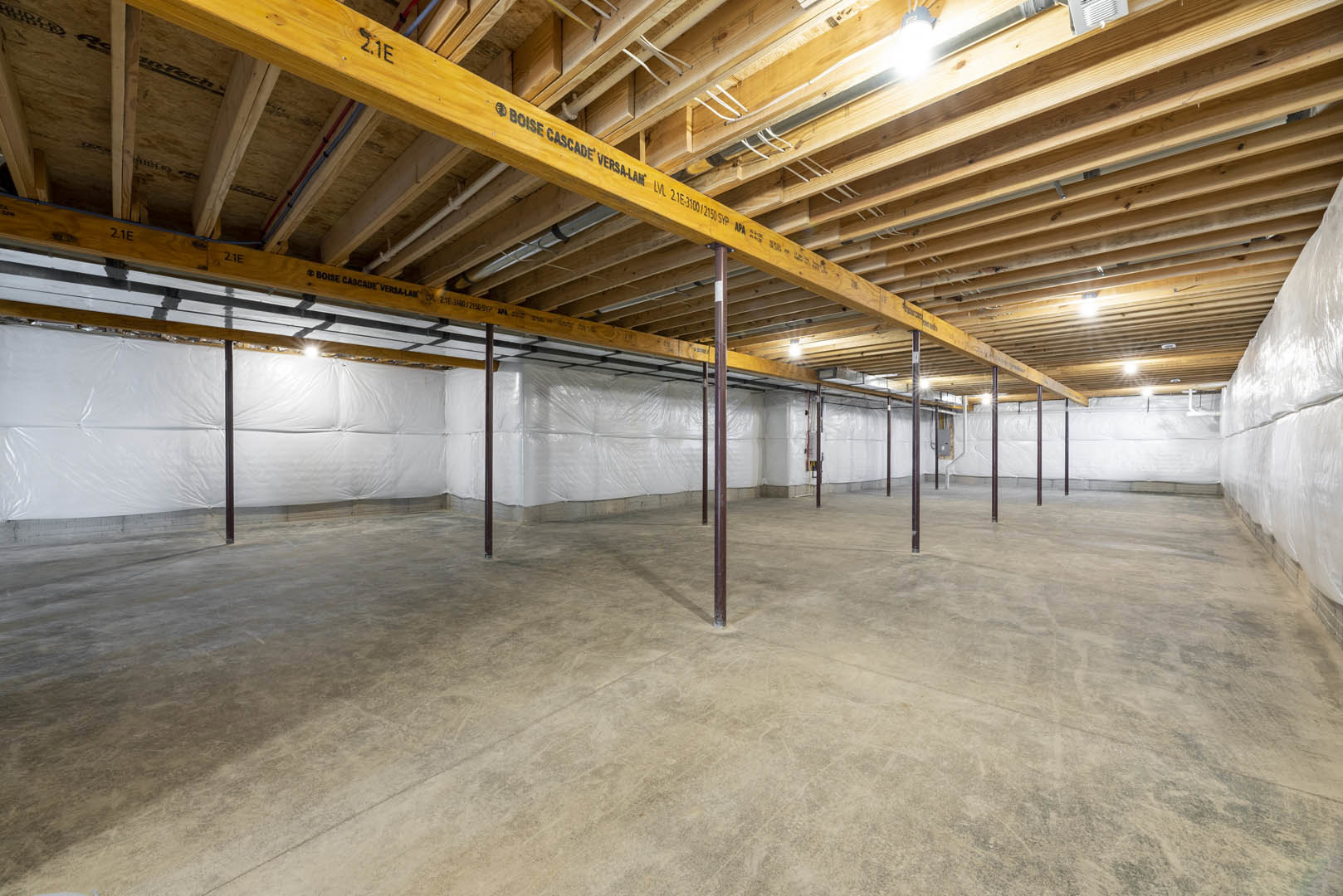 Open room with exposed wooden ceiling beams, concrete floor, steel support poles, and white composite wall panels