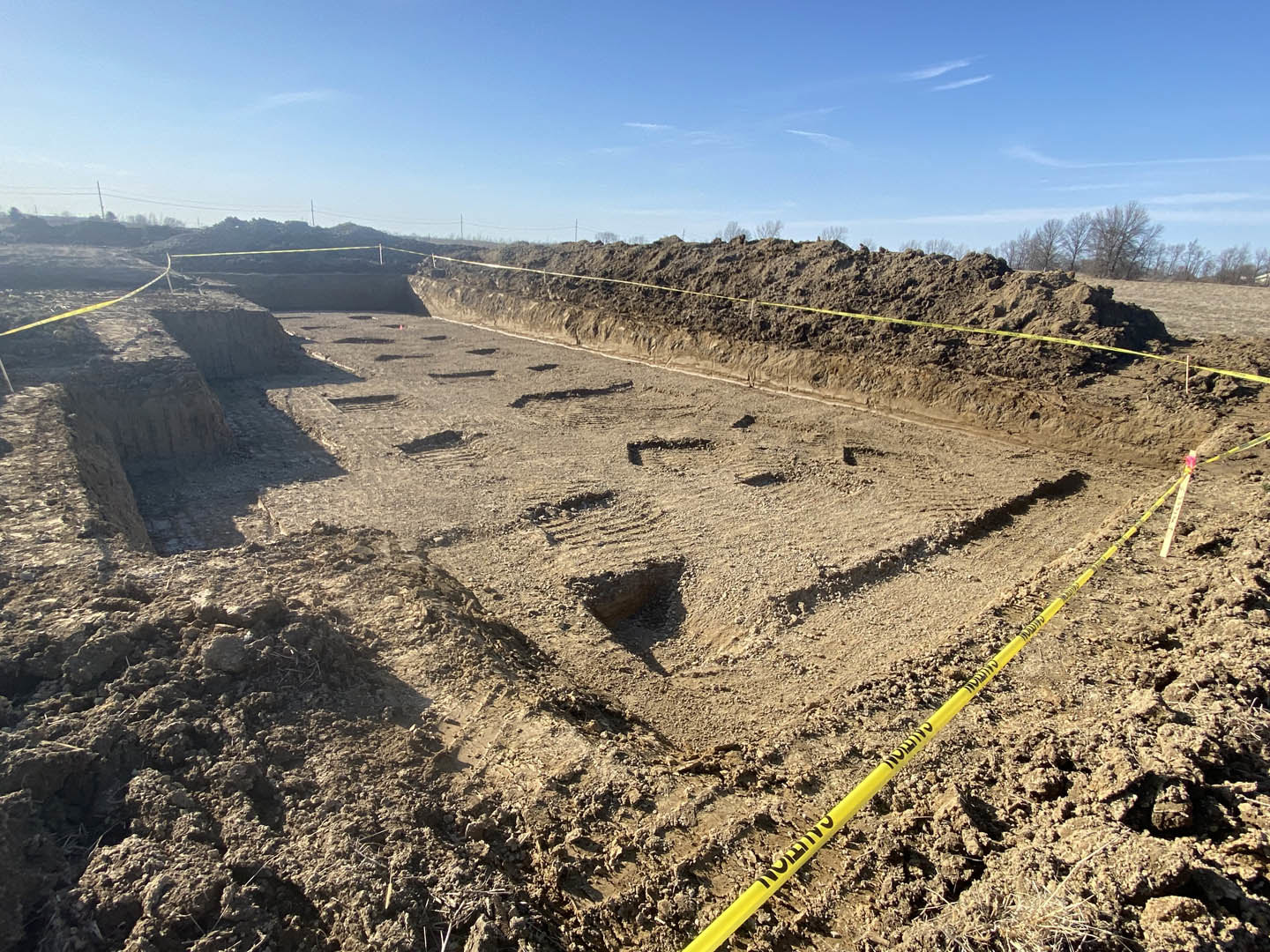 Yellow caution tape stretched across dirt mound at residential construction site under blue sky with scattered clouds