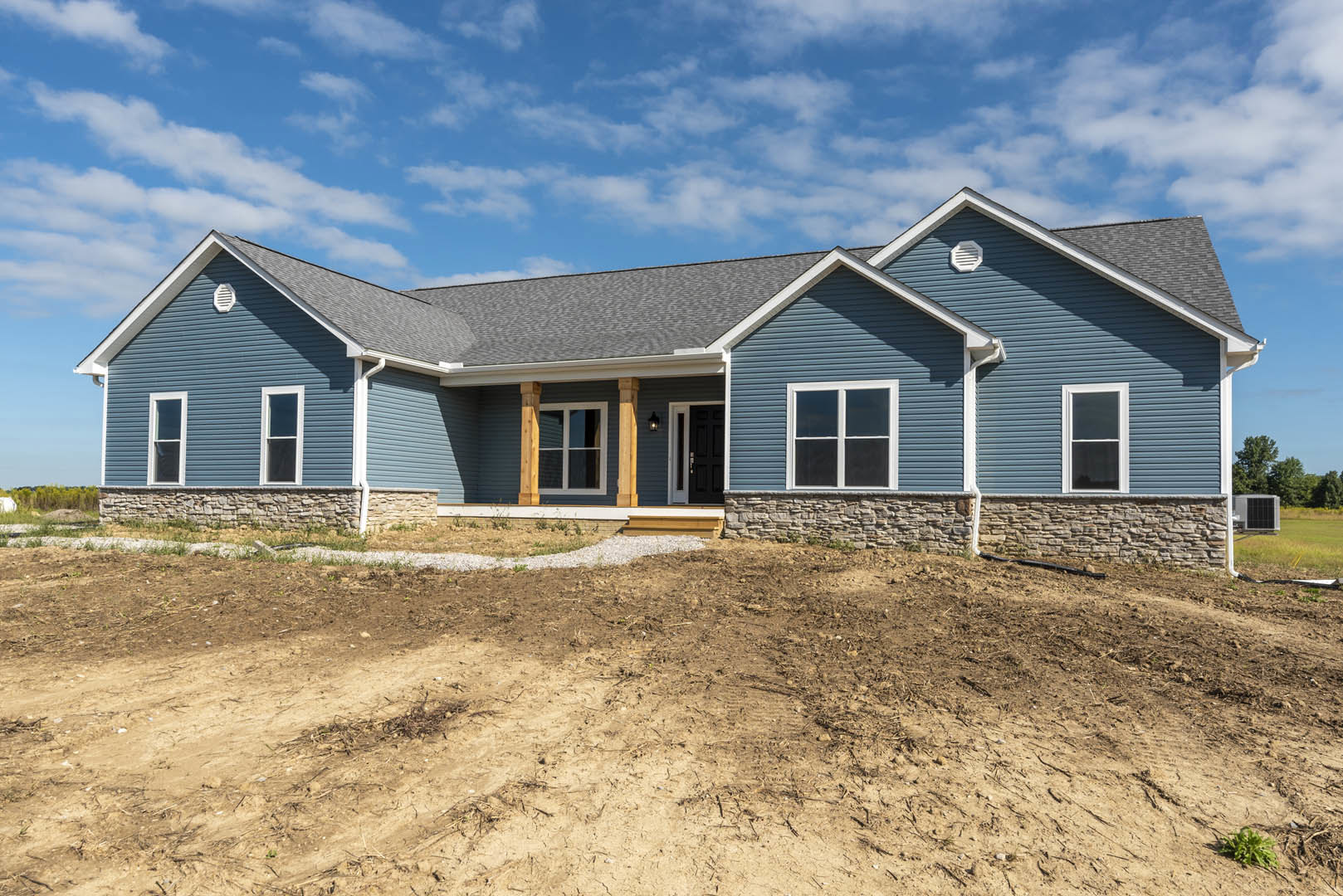Blue house with white-trimmed windows, black front door, stone accent wall, and dirt landscaping in front.