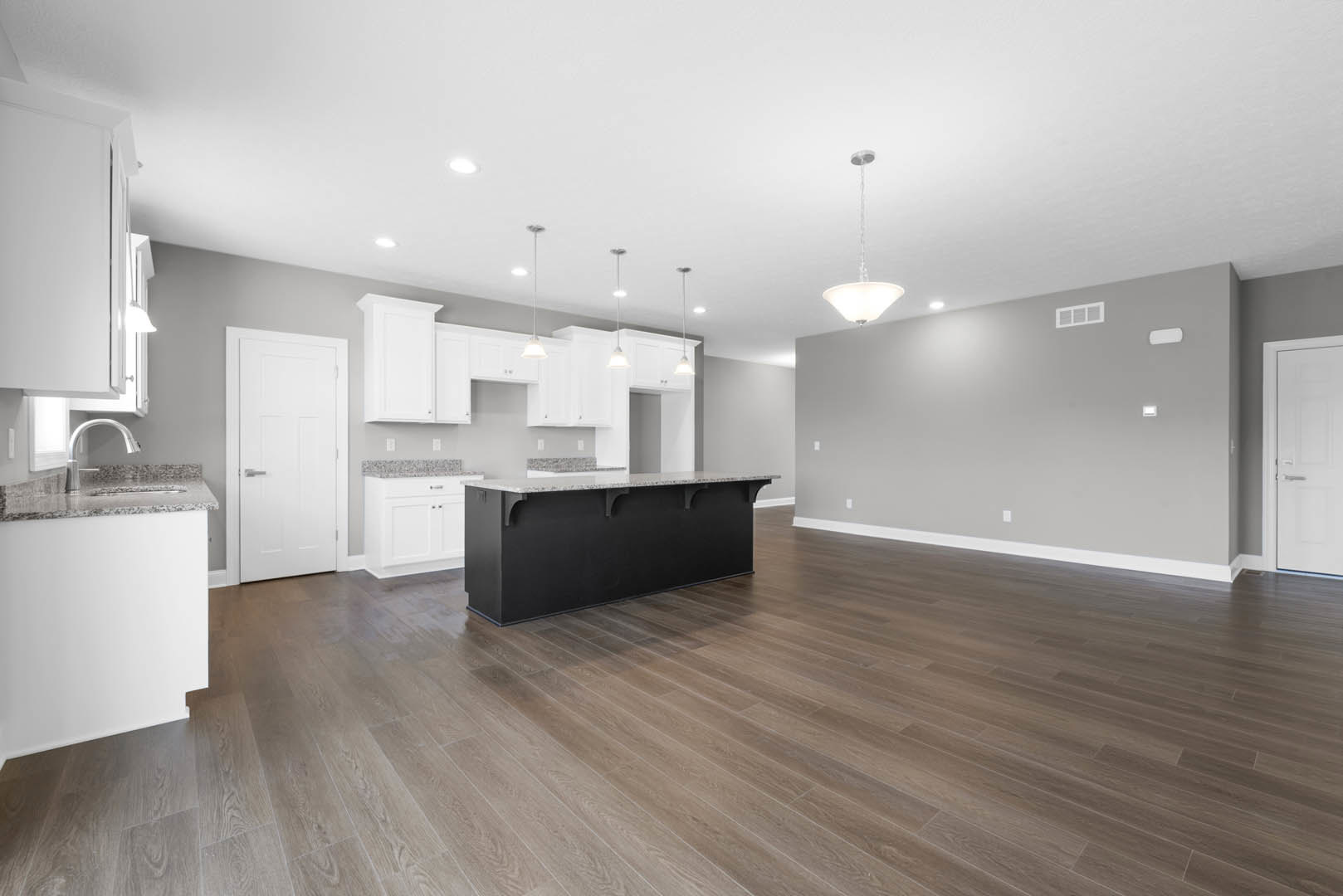 Open kitchen and dining area with hardwood flooring, black island topped with white countertop, white cabinetry, and white doors featuring silver handles