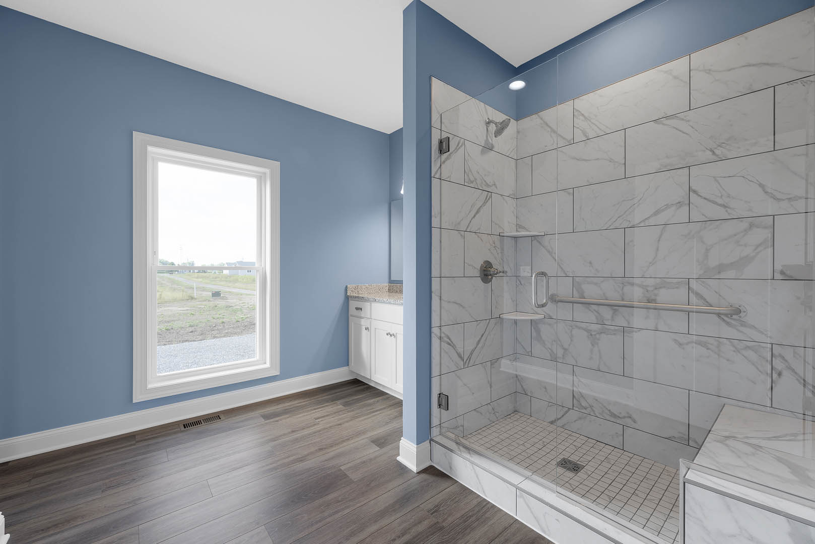 Bathroom with glass shower enclosure, wood plank flooring, marble countertop, chrome faucet, and window overlooking grassy field