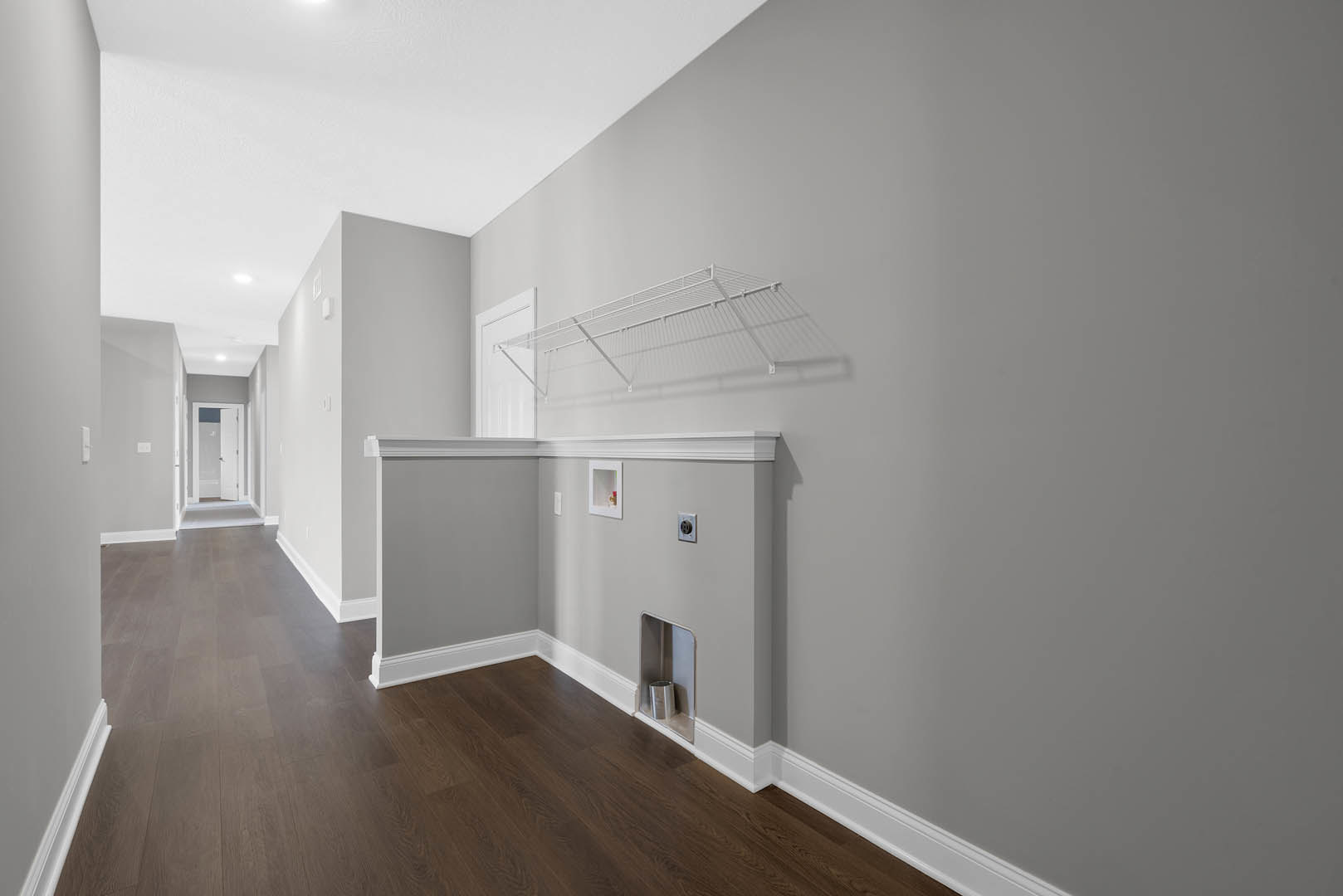 Hallway with white wall-mounted shelf, white railing, silver trash can in corner, white door with window, wood laminate flooring, plaster walls