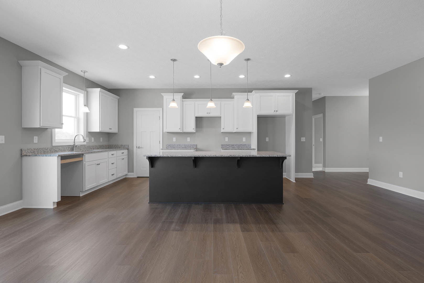 Spacious kitchen featuring a large black island countertop, surrounding white counters, wood flooring, black accent wall, modern light fixture, stainless steel faucet, and white