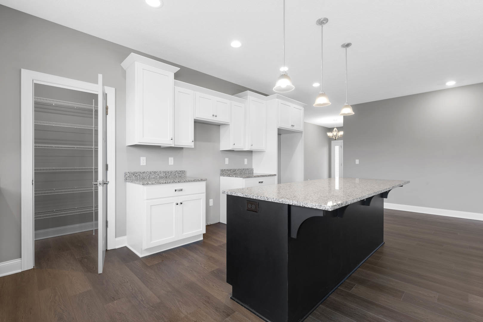 Black kitchen island with waterfall countertop, white shaker cabinets, stainless steel sink, pendant light fixture, light hardwood flooring, and granite surfaces.